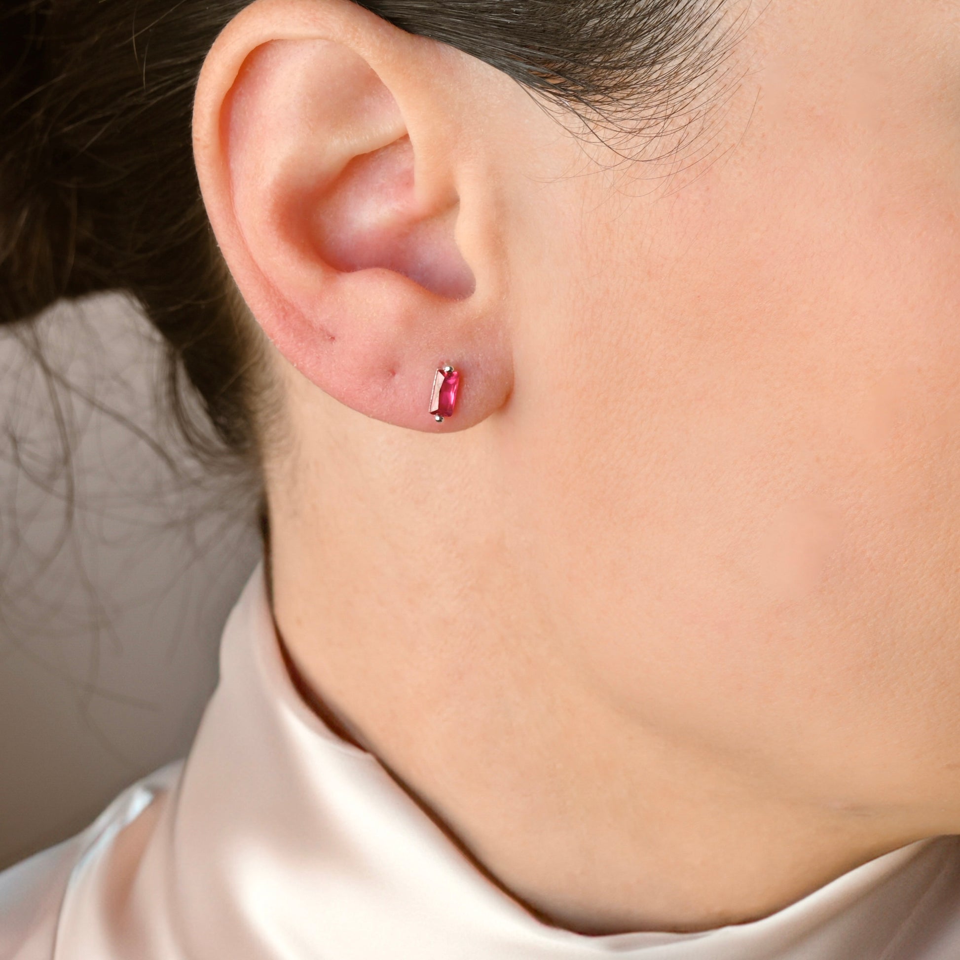 Close-up of an ear with a silver baguette stud earring with dark pink stone.