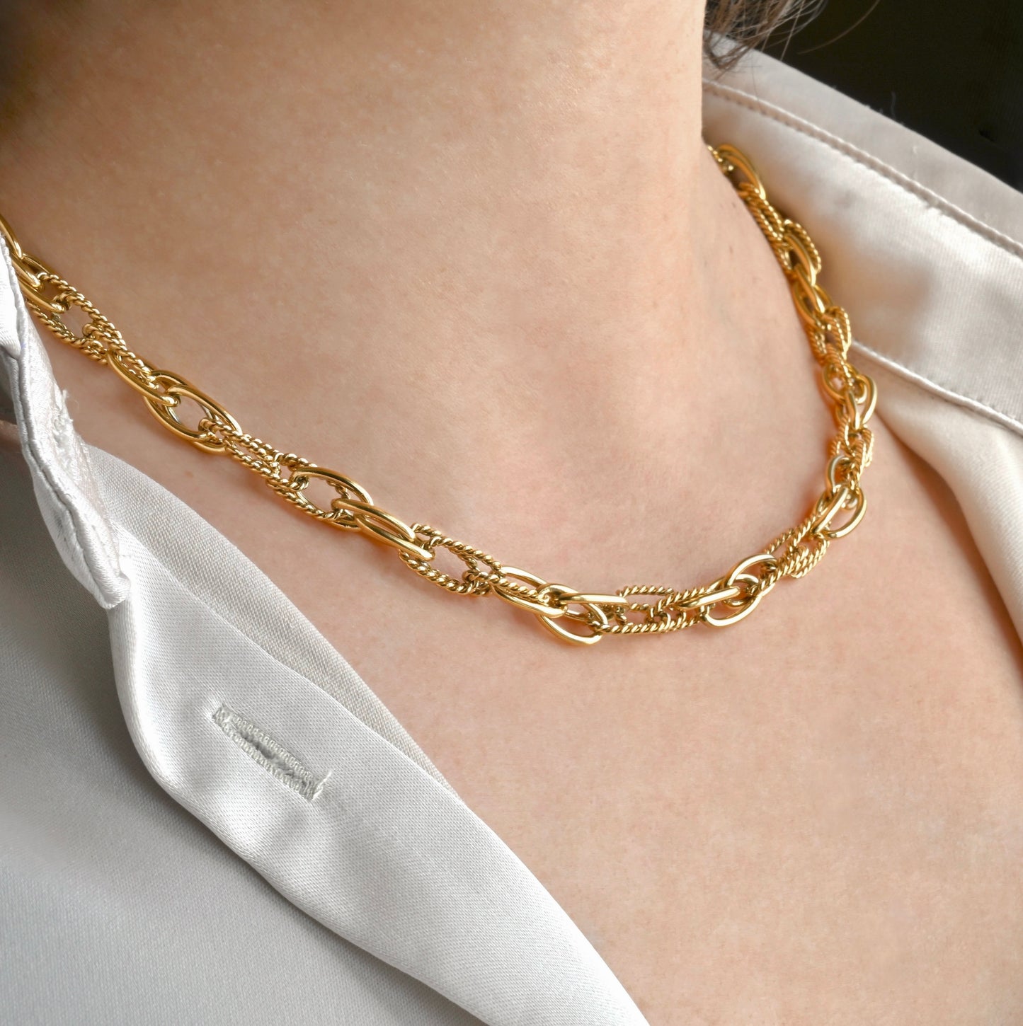 Gold chain necklace with interlocking smooth polished and twisted oval links worn by a person in gray shirt