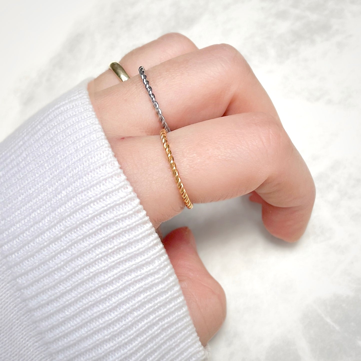 Hand wearing two twisted rings, one gold one silver, on a white background