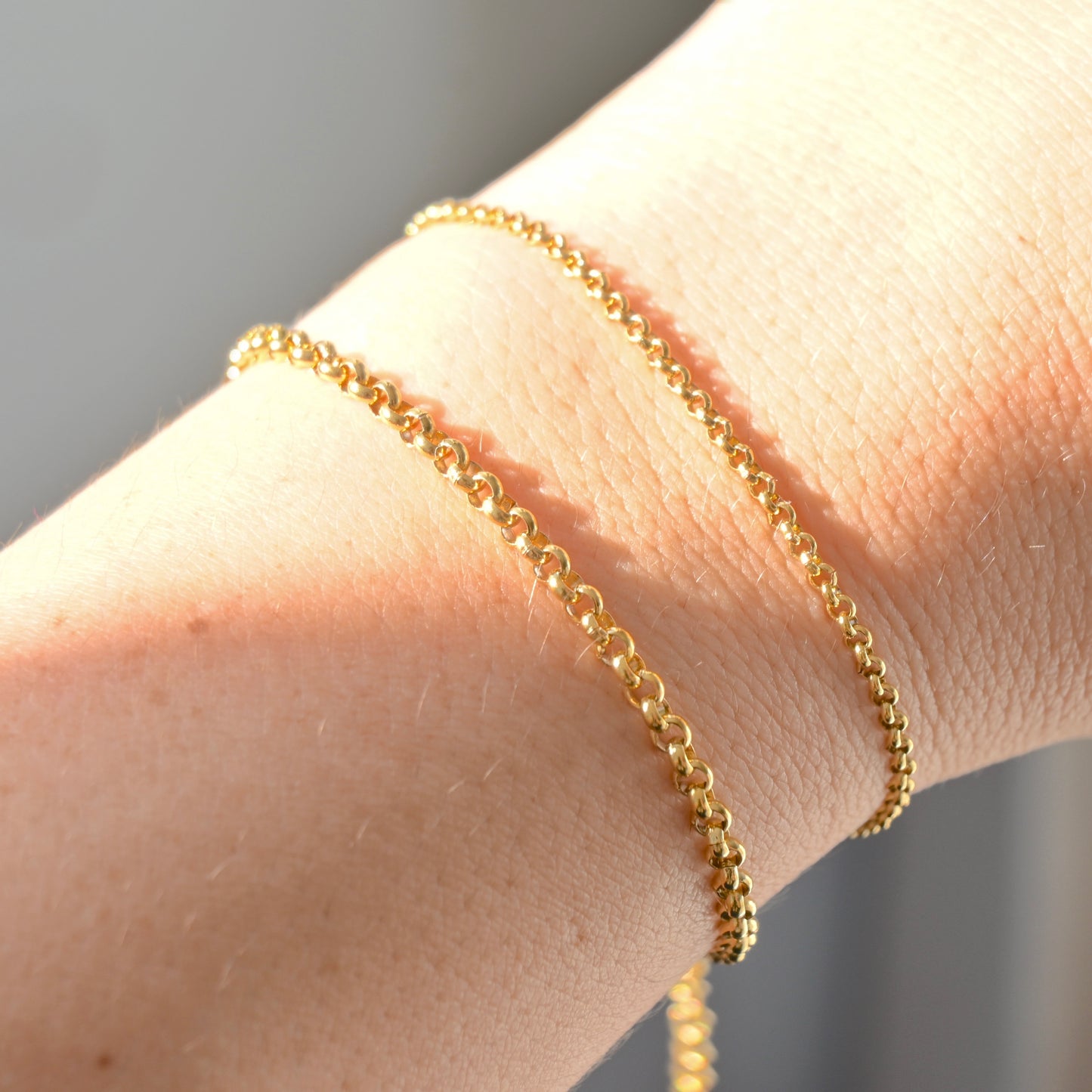 Gold bracelets on a wrist with a neutral background under direct sunlight
