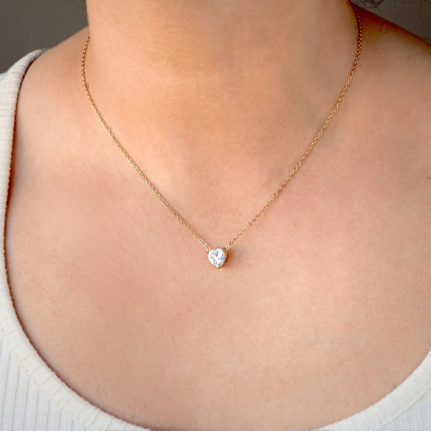 Gold necklace with a white heart diamond pendant on a person wearing a white top.