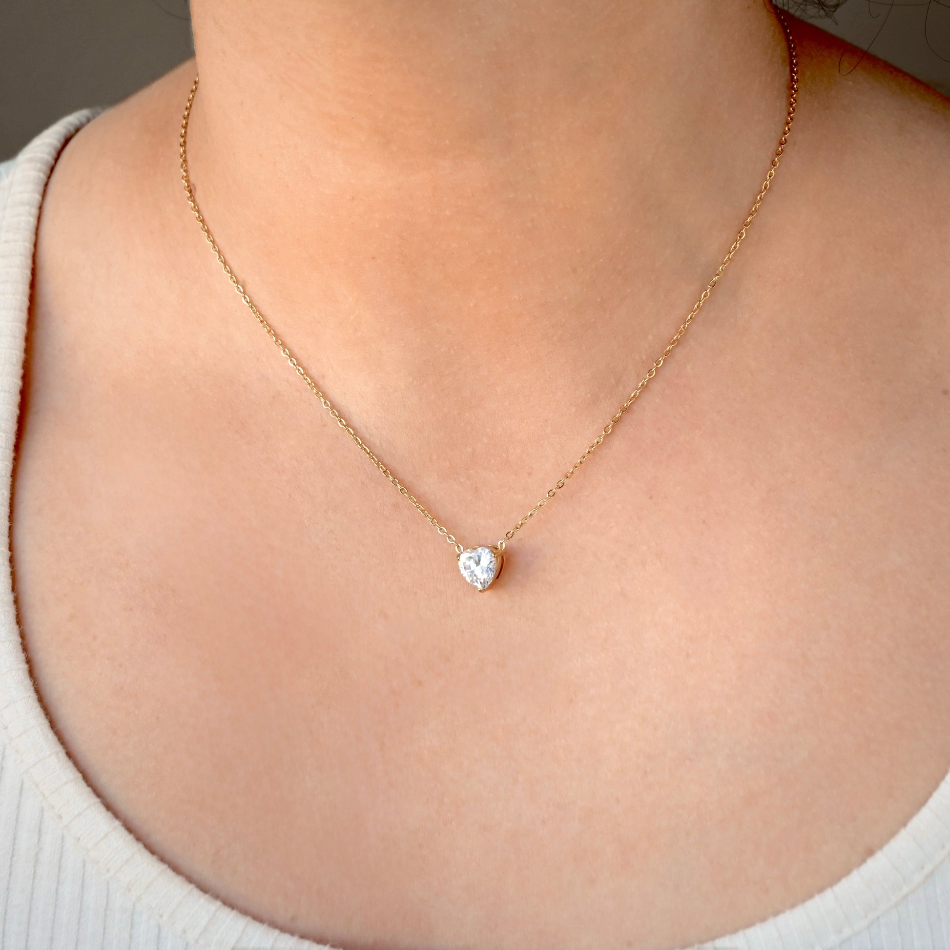 Gold necklace with a white heart diamond pendant on a person wearing a white top.