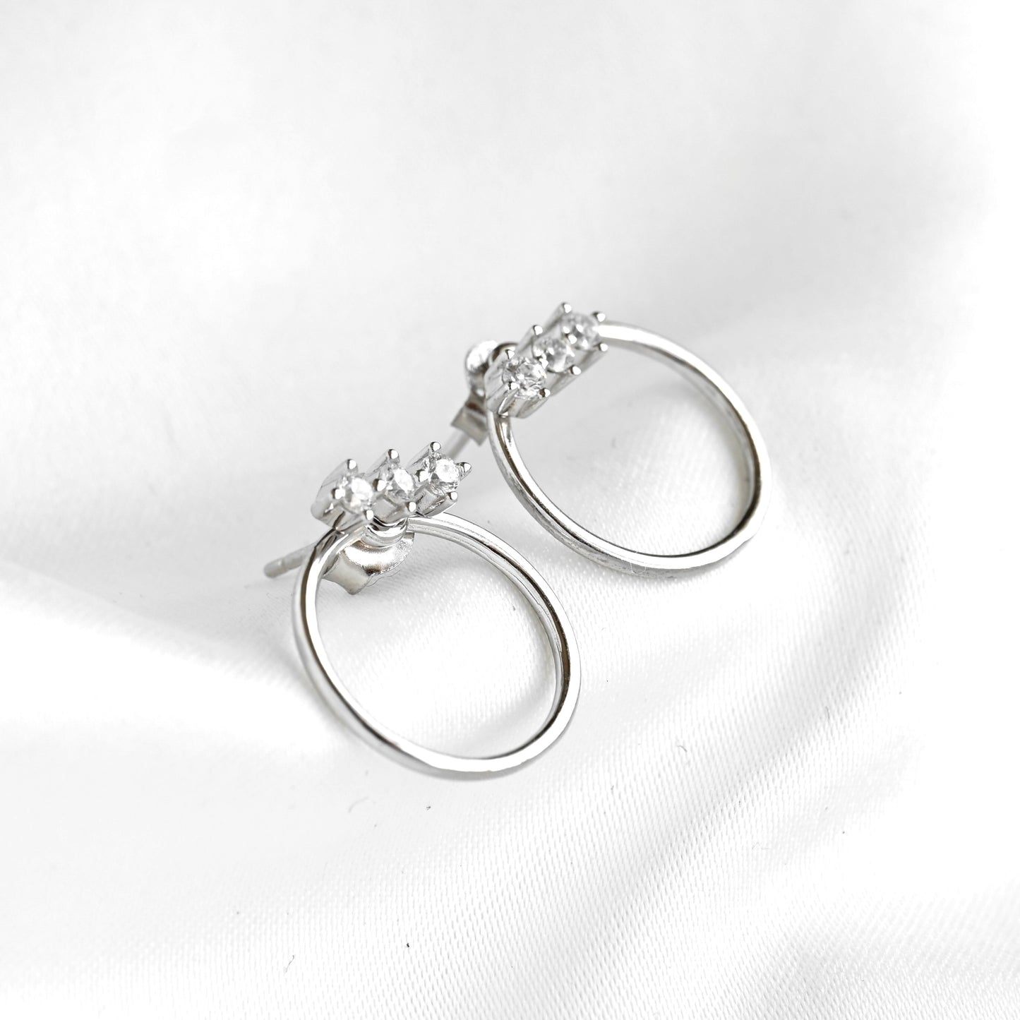Pair of silver hoop earrings with clear gemstones on a white background