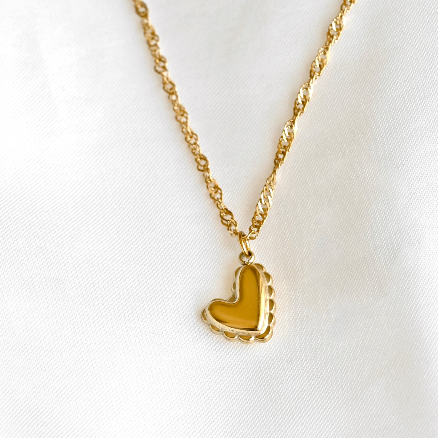 Gold heart necklace on a dainty twisted chain on a white background