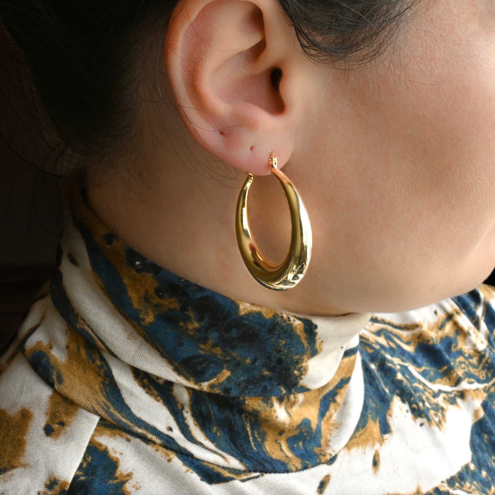 Large Gold dome hoop earrings worn by a person with a patterned garment.