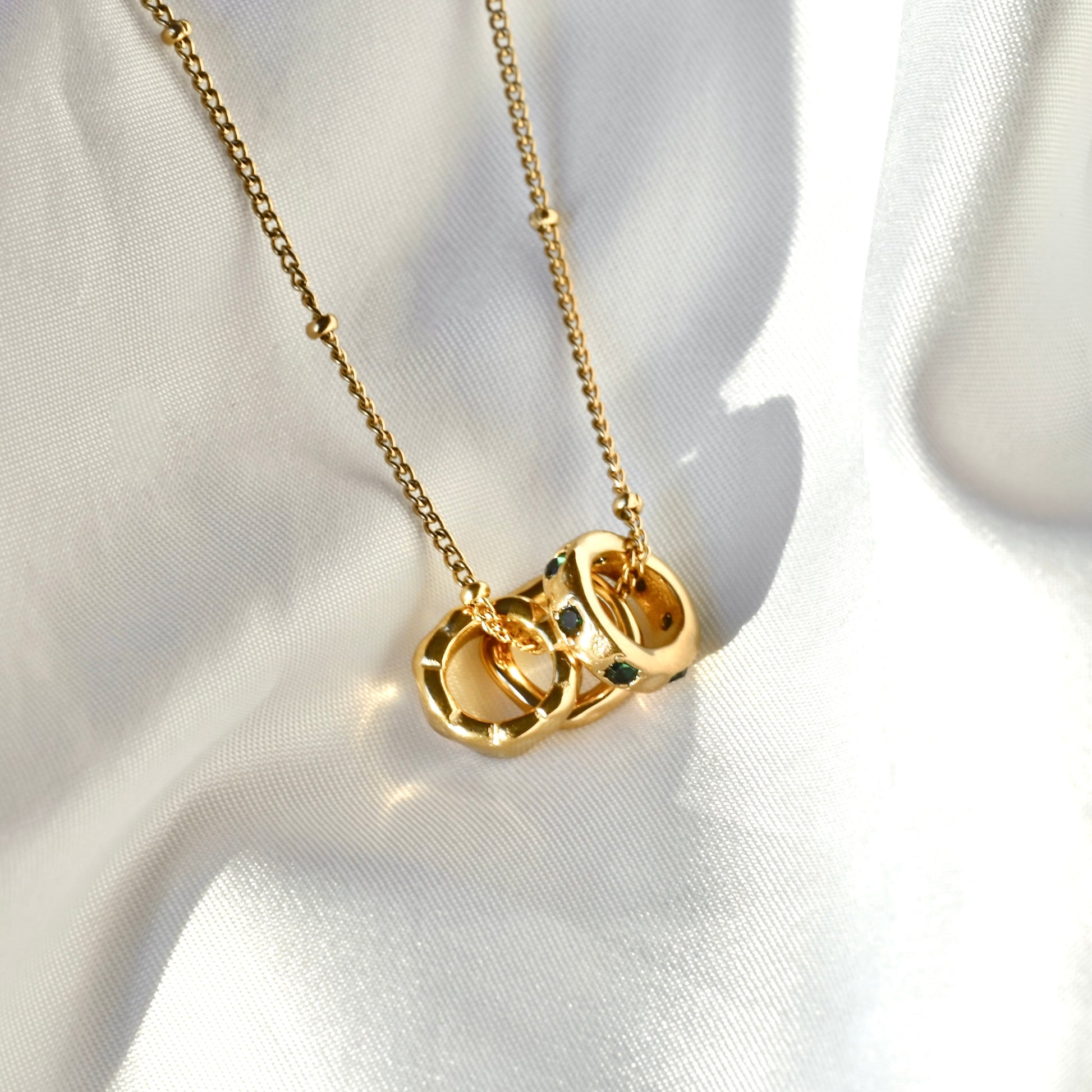 A gold chain necklace with a pendant made of interlocking open rings, photographed on draped white fabric.