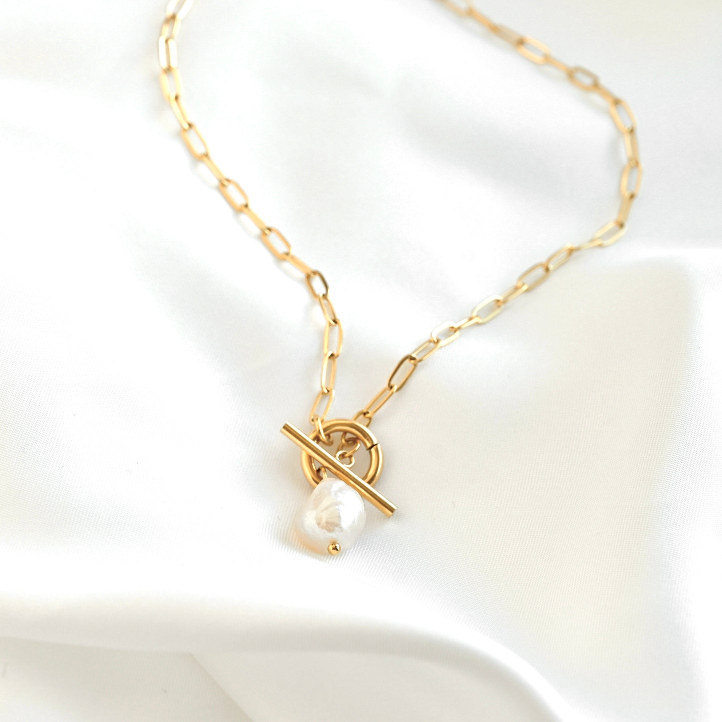 Gold paperclip necklace with a pearl pendant on a white background