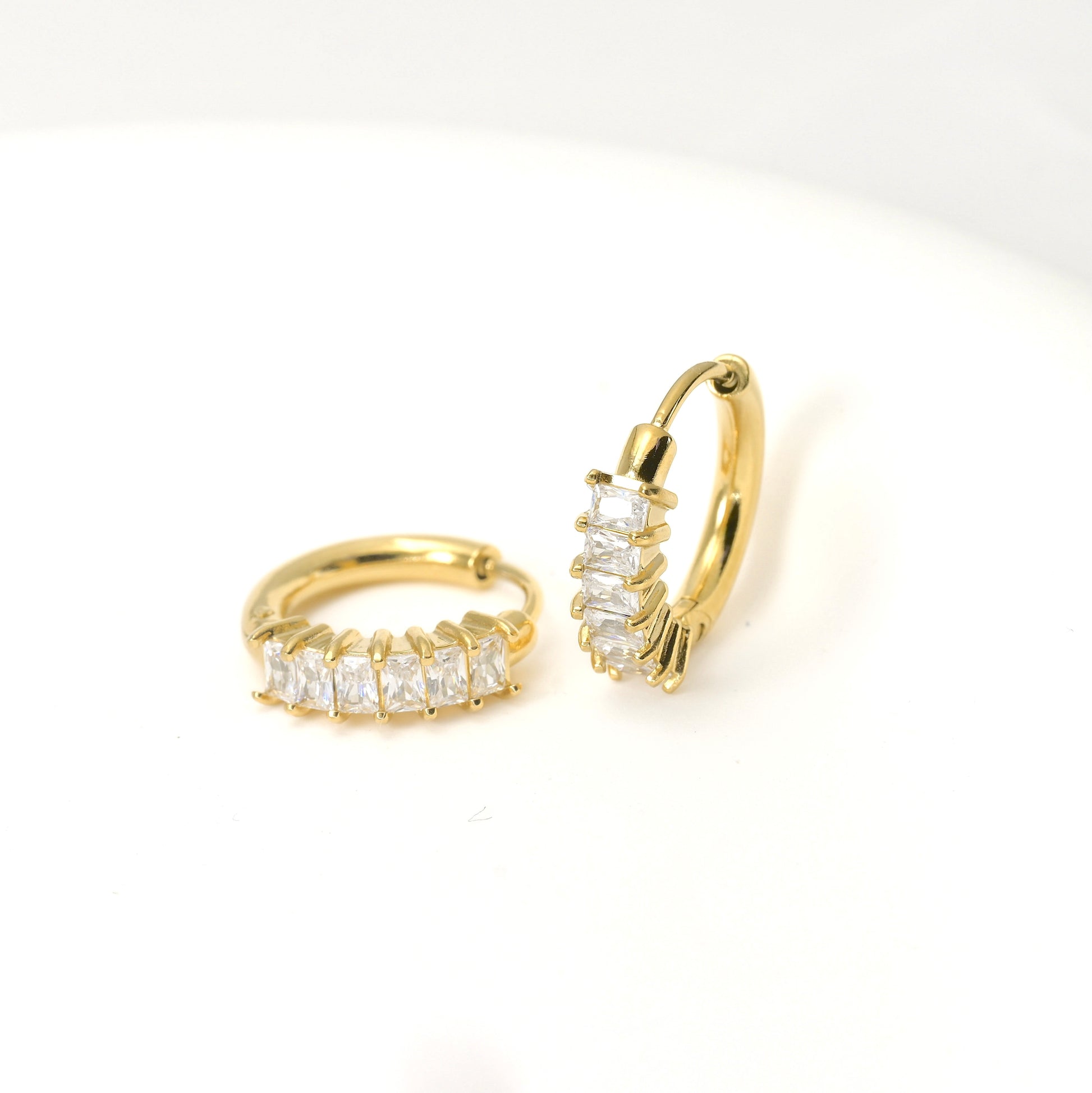Gold hoop earrings with clear rectangular gemstones on a white background