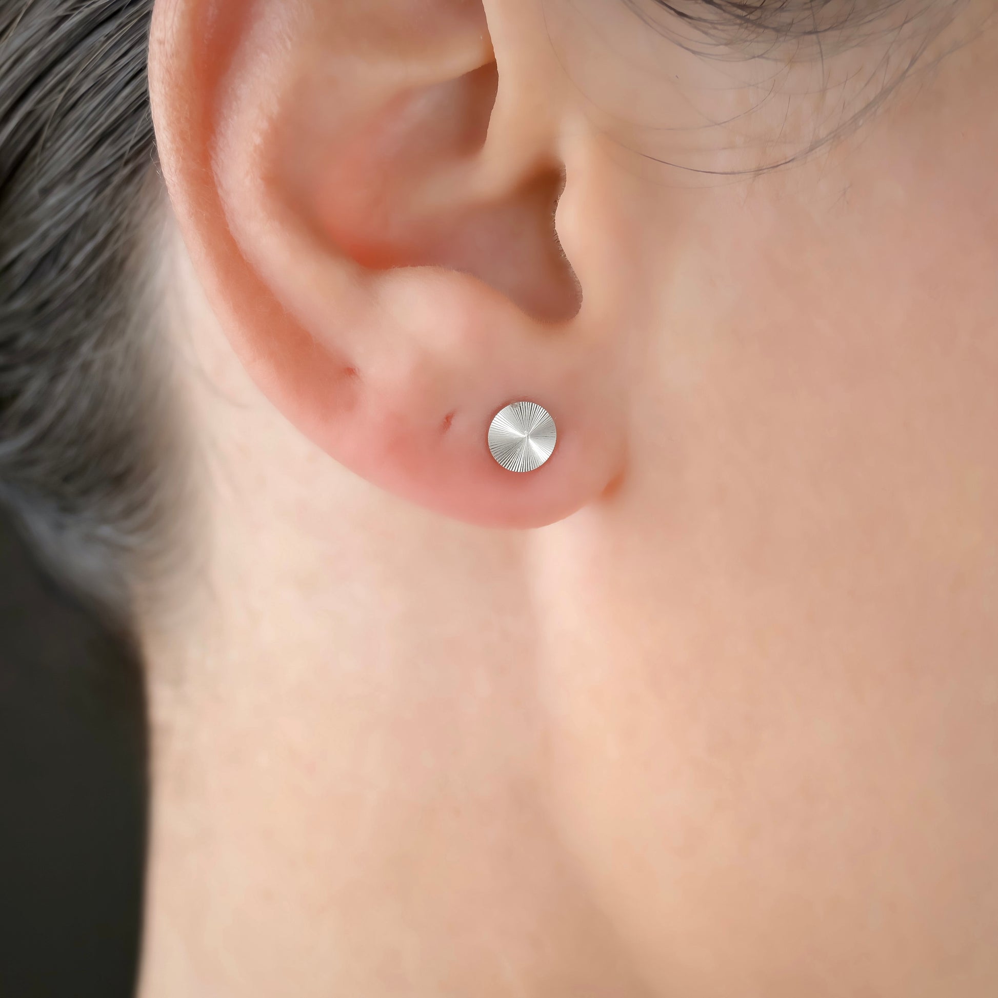 Close-up of a person wearing a silver round stud earring.