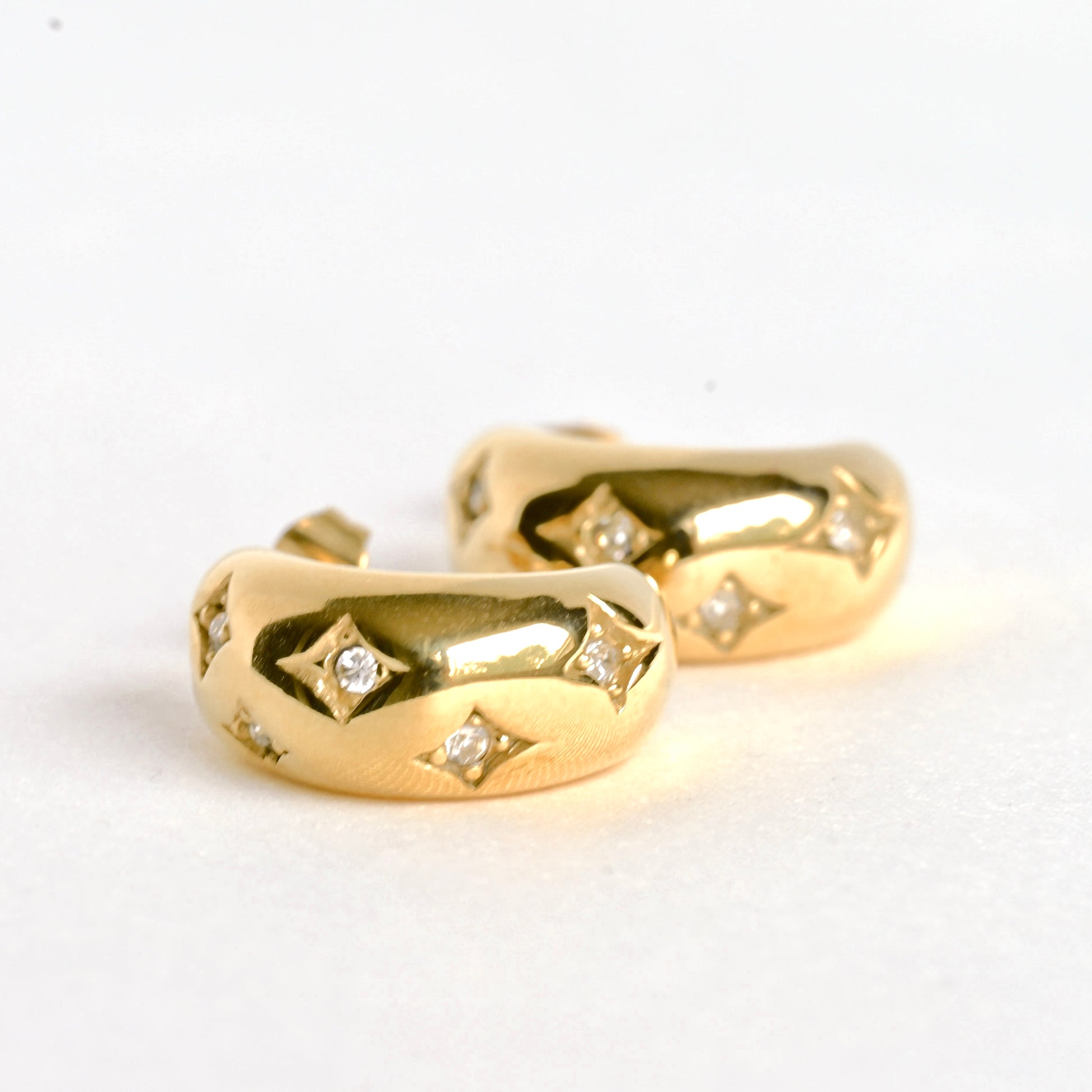 Gold hoop earrings with embedded diamonds resembling stars on a white background