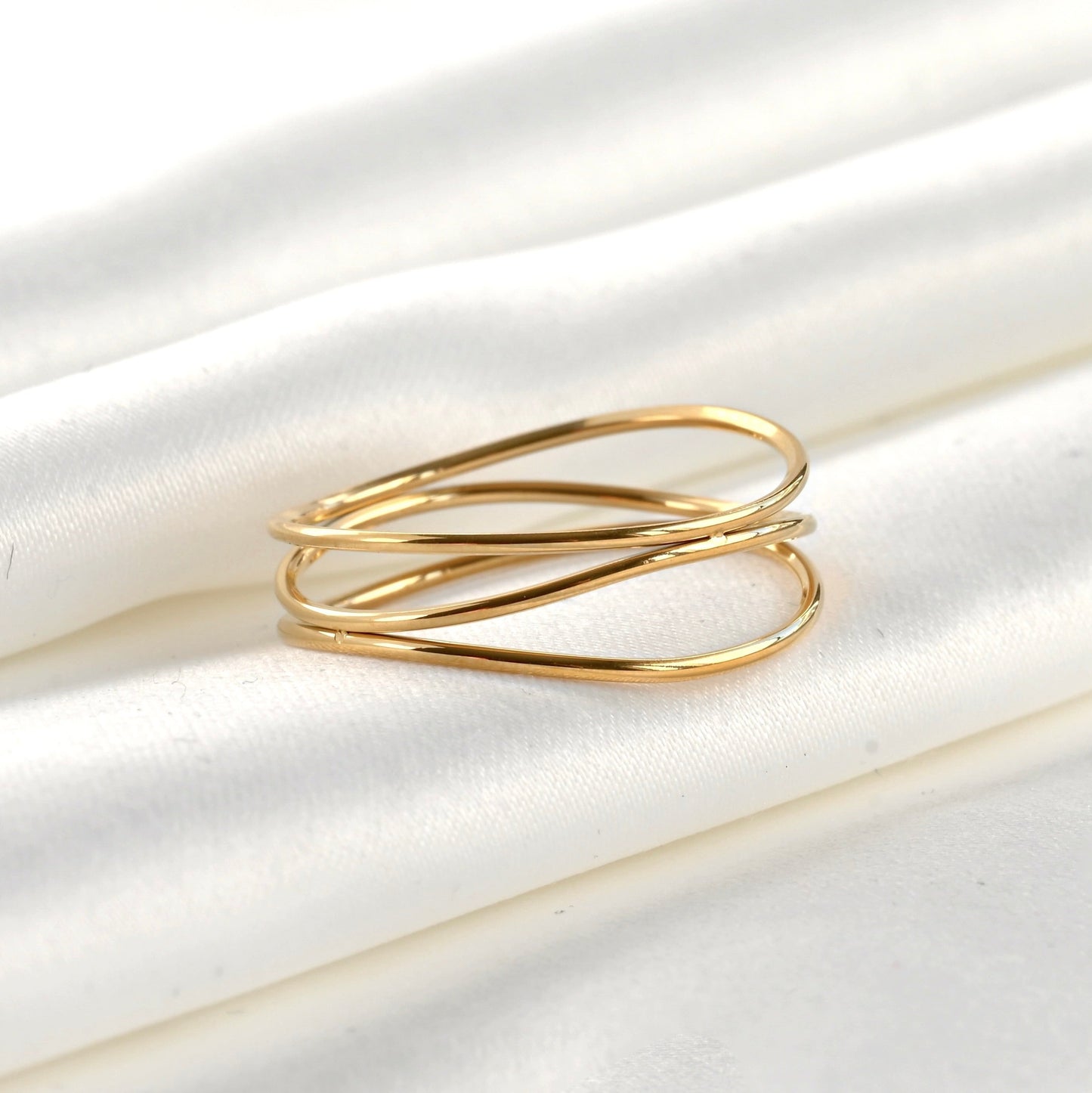 Gold ring with three wavy intertwined bands on a white fabric background