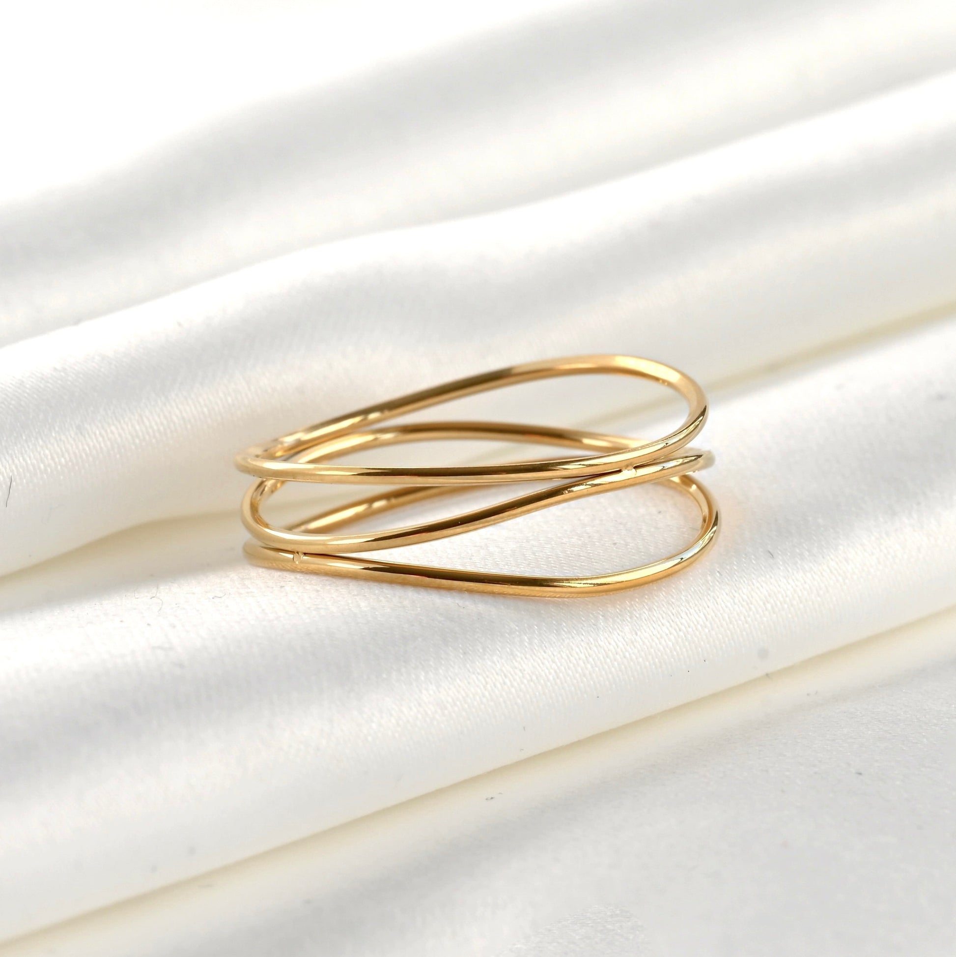 Gold ring with three wavy intertwined bands on a white fabric background