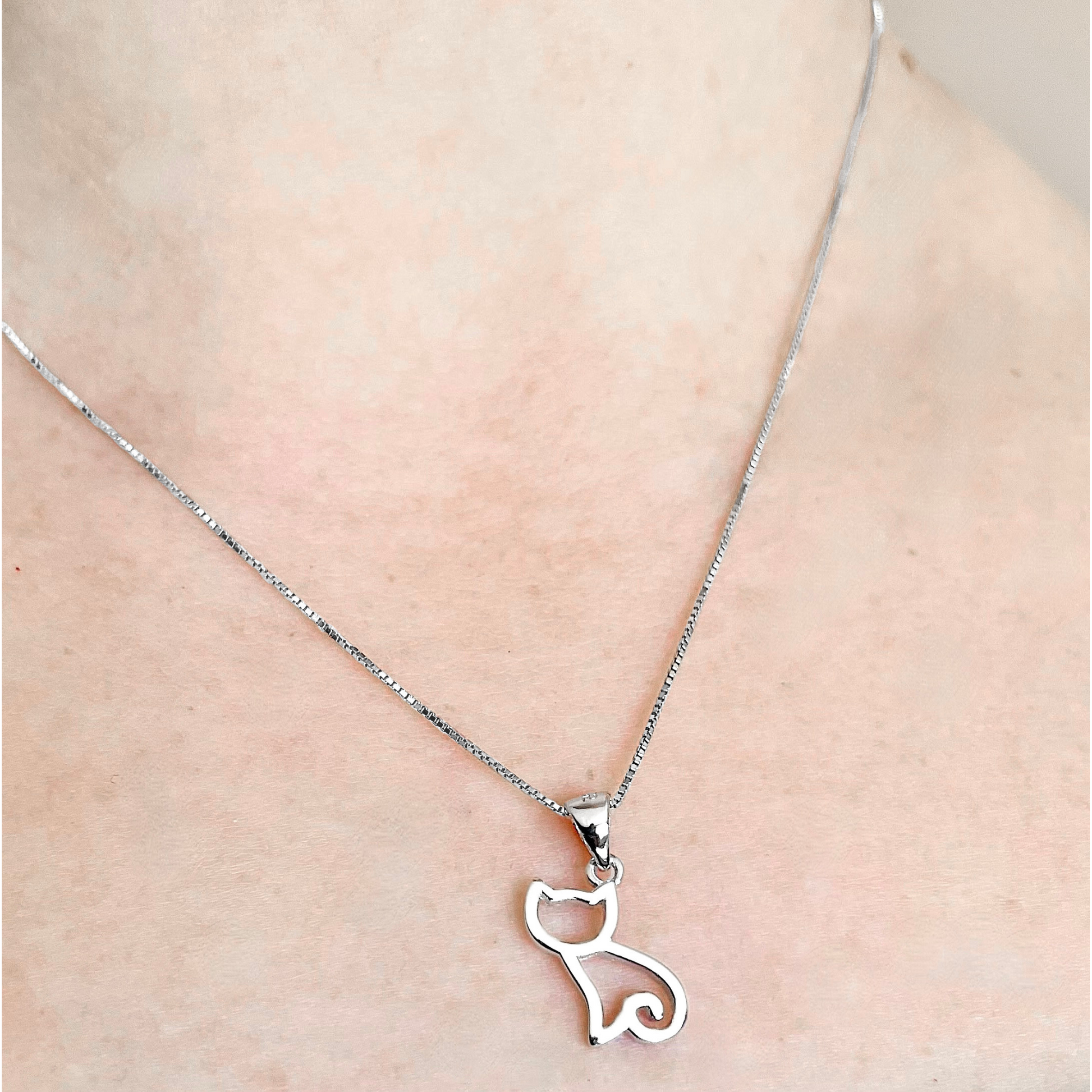Silver cat pendant necklace on a person's neck against a neutral background