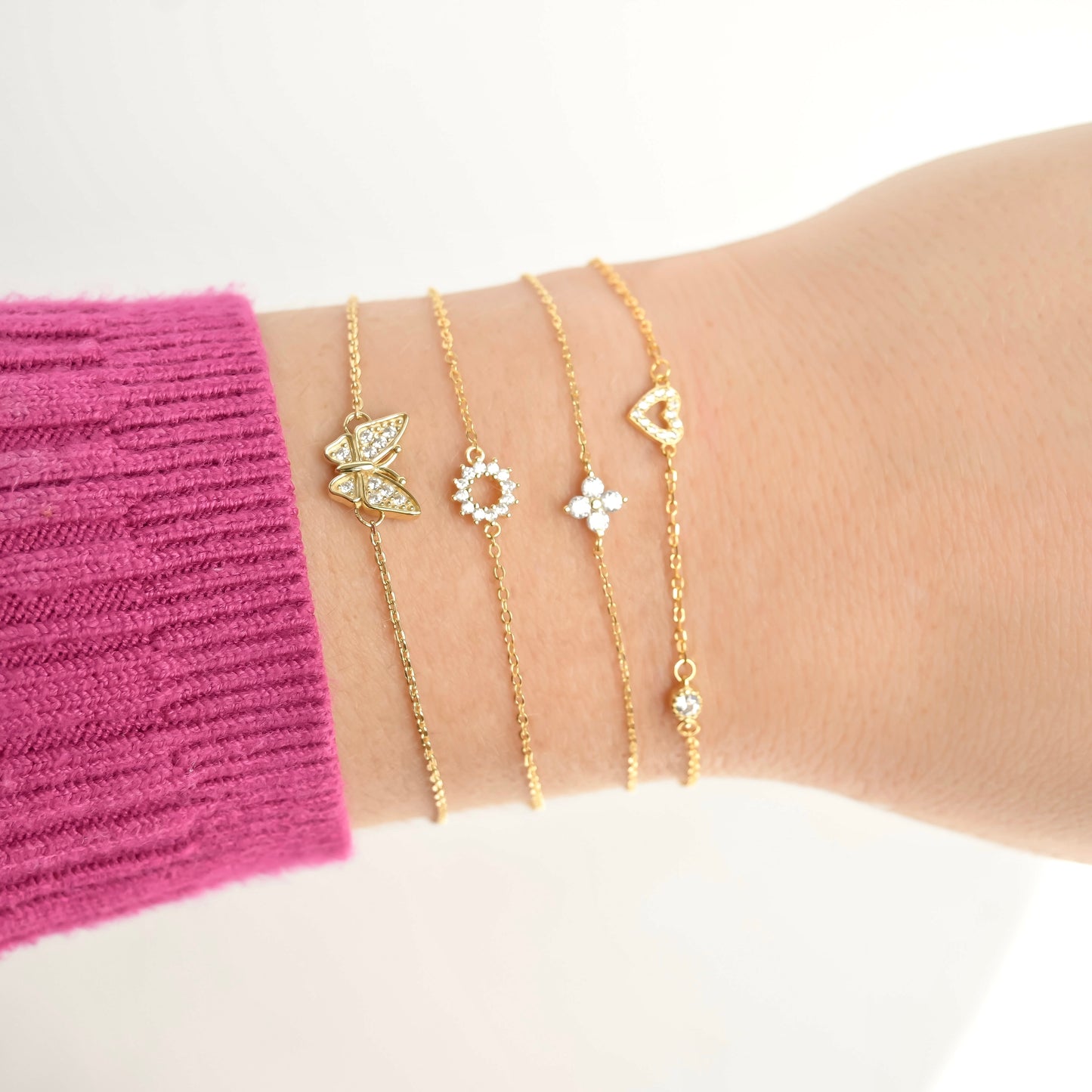 Side view of a wrist wearing gold bracelets with butterfly and heart designs 