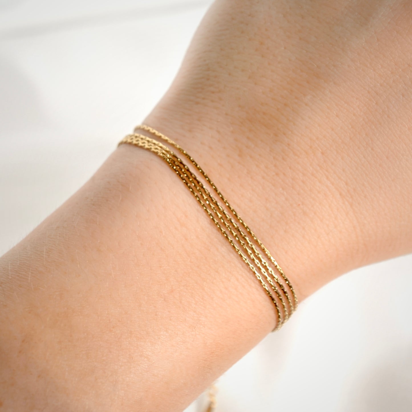 A close-up of a delicate gold chain bracelet worn on a person's wrist, showing three parallel fine chains against light skin.