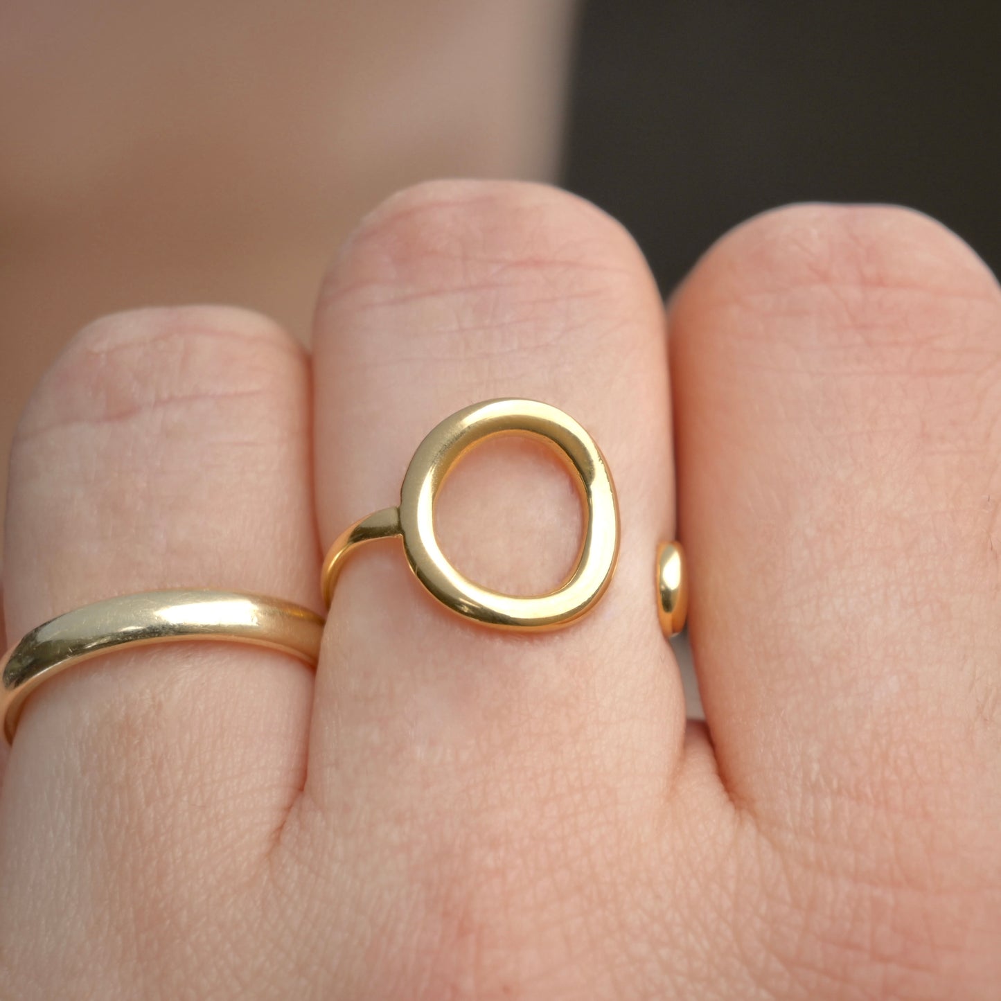 Gold concave cirlce ring with a unique design on a finger against a blurred background