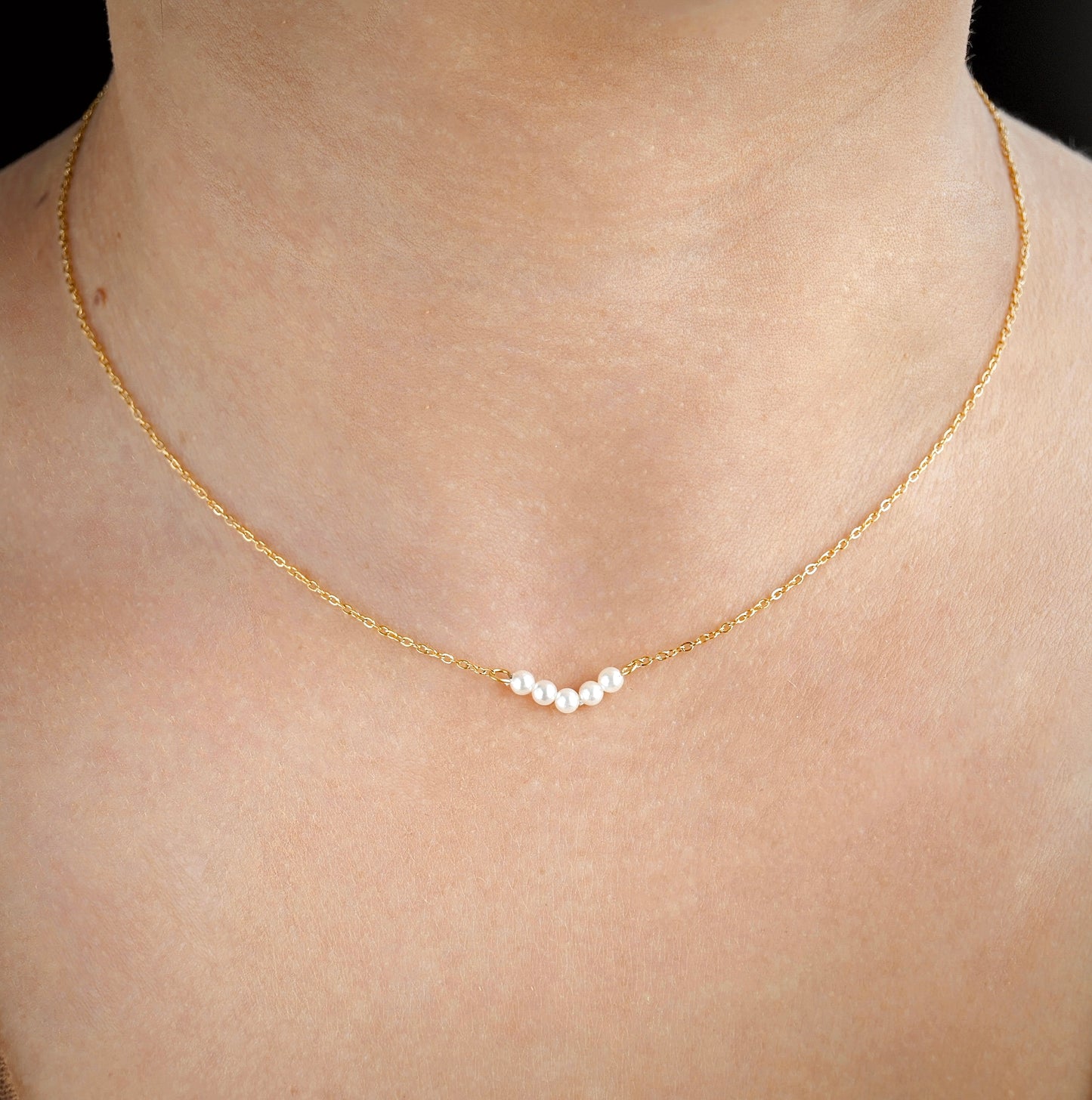 Gold necklace with small pearls on a person's neck against a neutral background