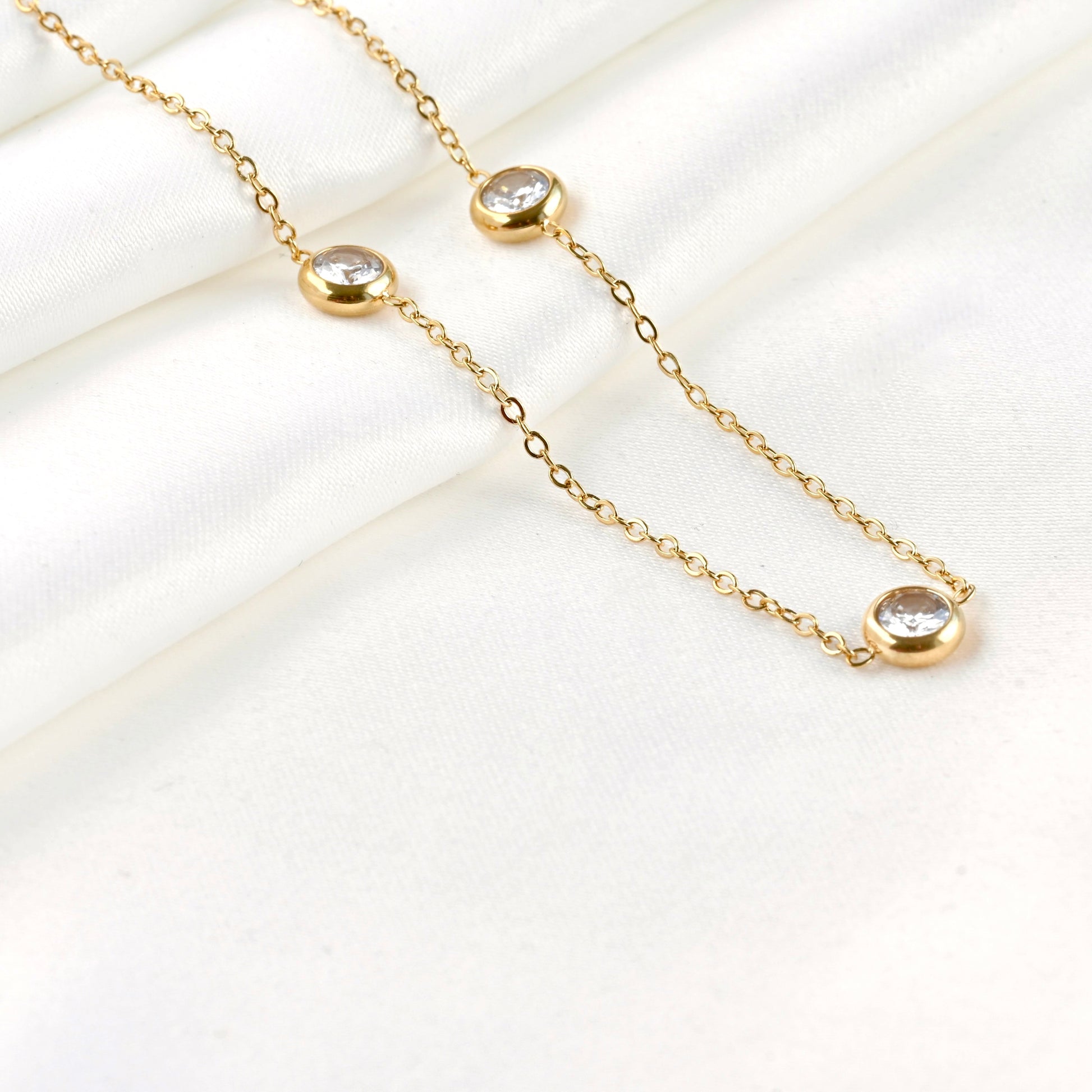 Close up view of gold  bezel necklace with three crystal pendants on a white background