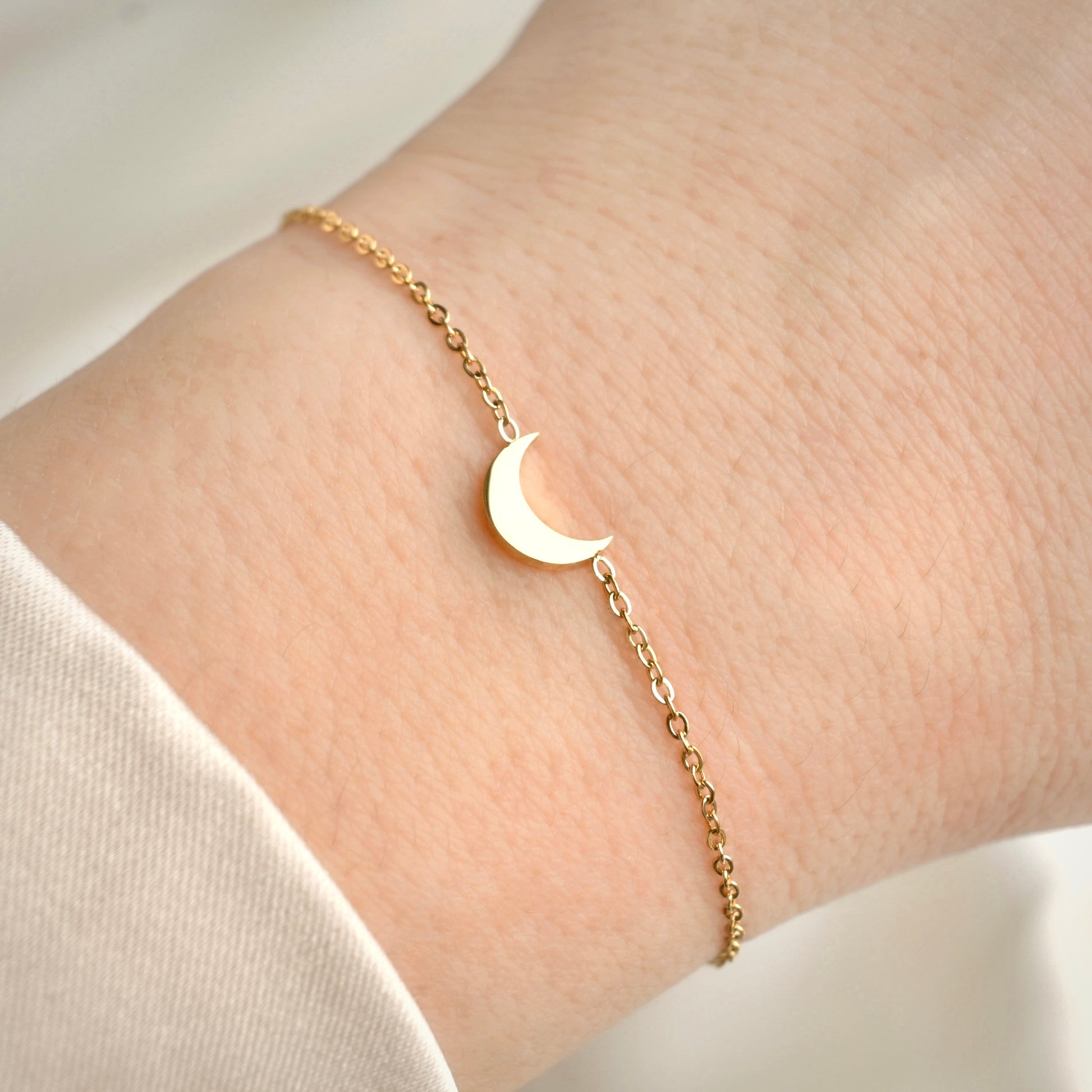 Gold bracelet with a moon charm on a wrist against a neutral background