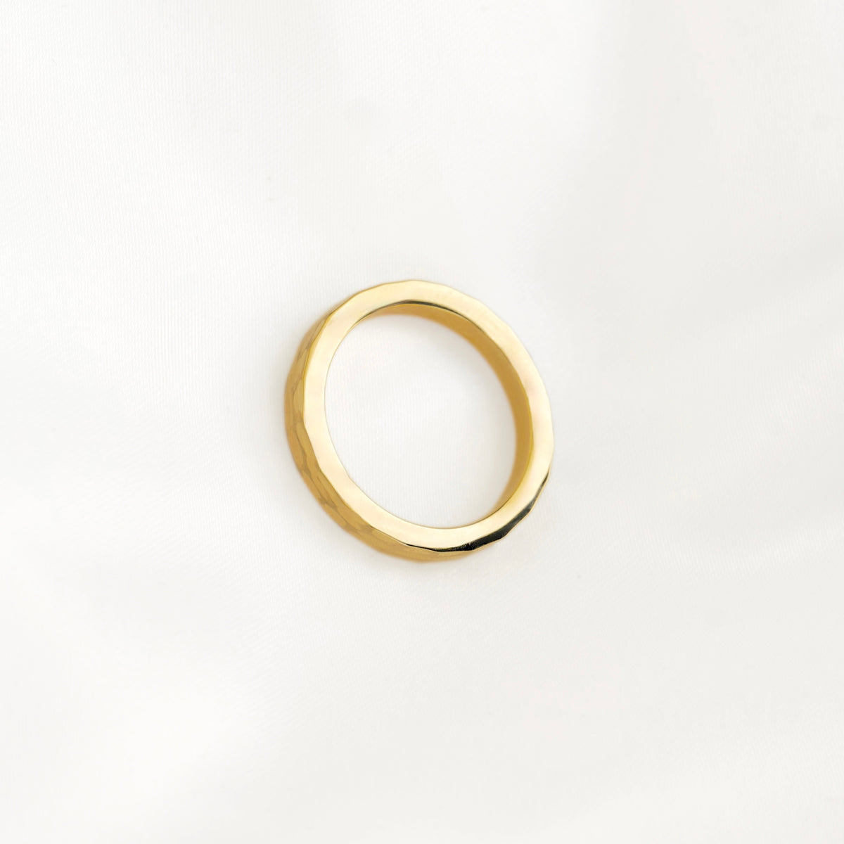 A polished gold ring with a slightly irregular, organic band, photographed on a clean white background.