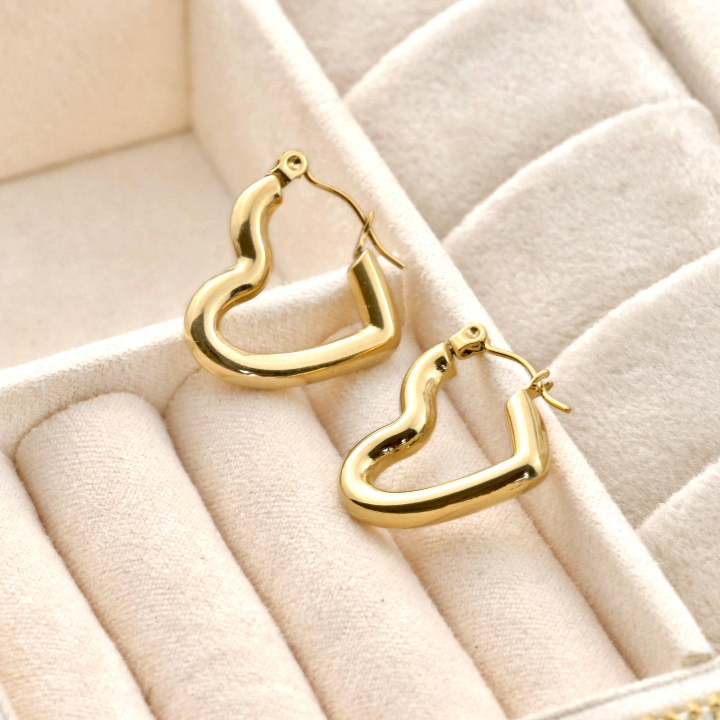 Gold tunnel heart-shaped earrings on a textured beige surface