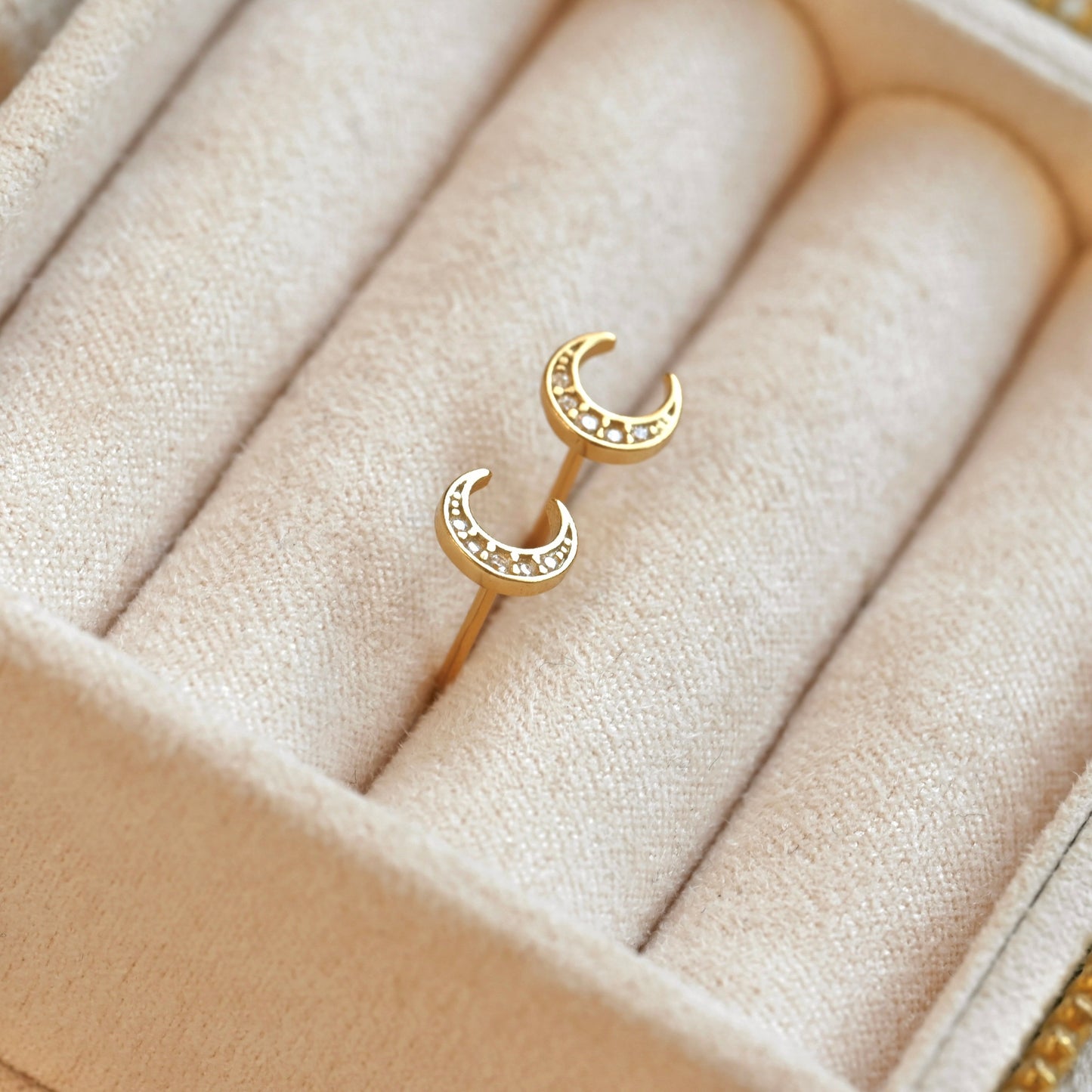Gold crescent moon earrings on a beige jewelry cushion