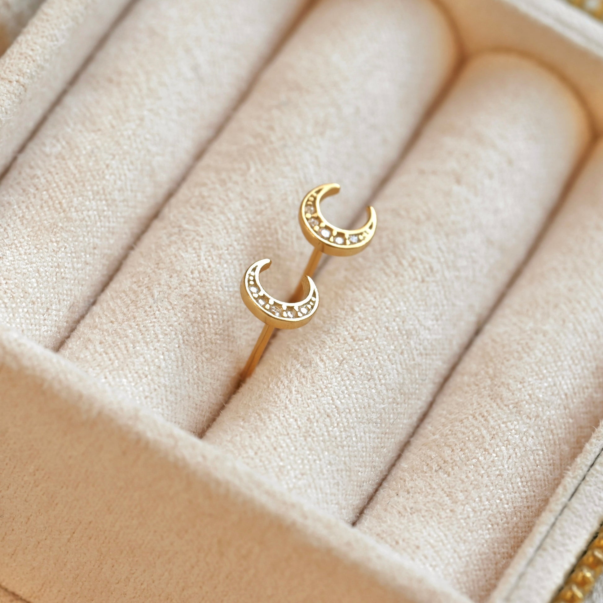 Gold crescent moon earrings on a beige jewelry cushion