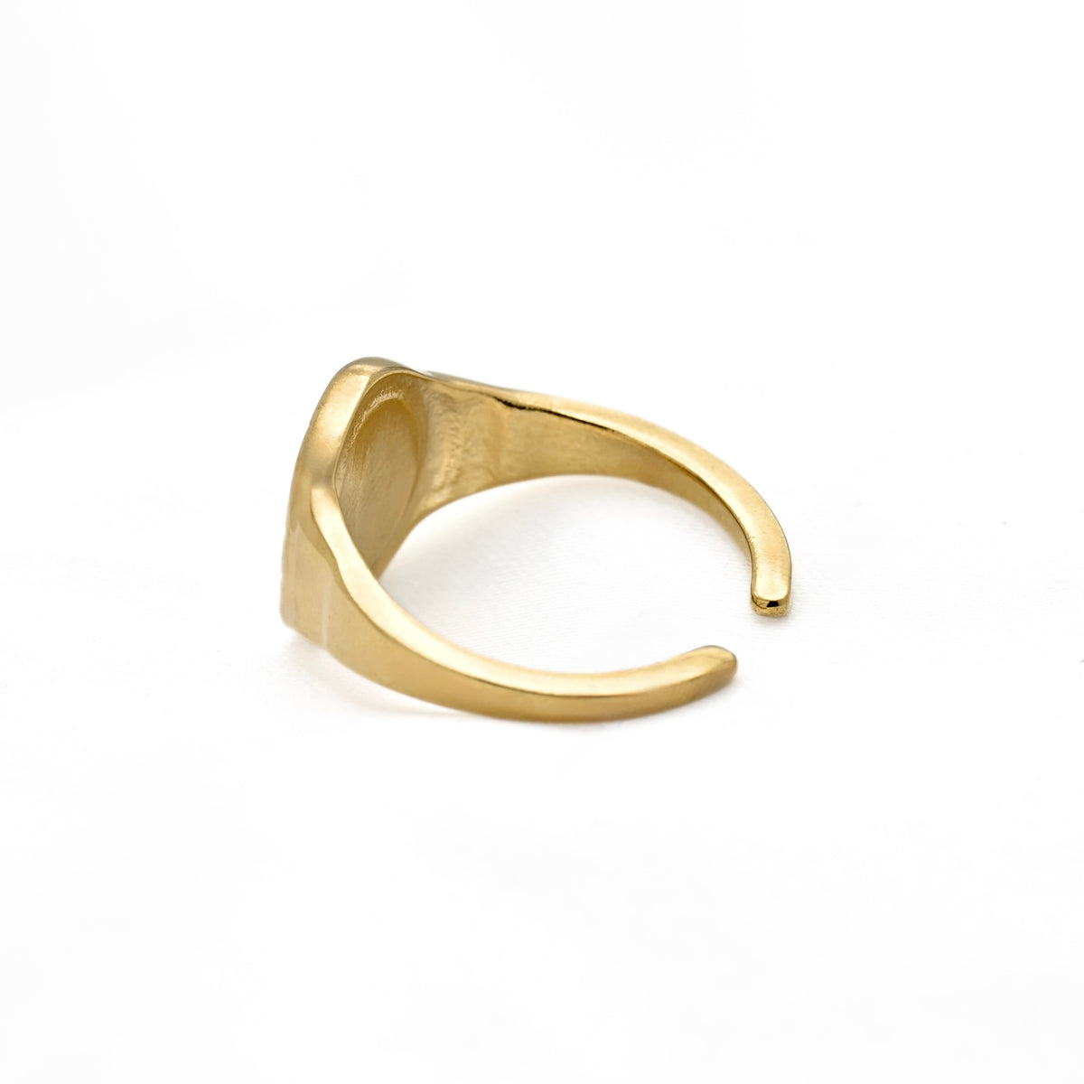 A gold signet-style ring with a wide, open band and a flat, slightly tapered face, photographed on a clean white background.