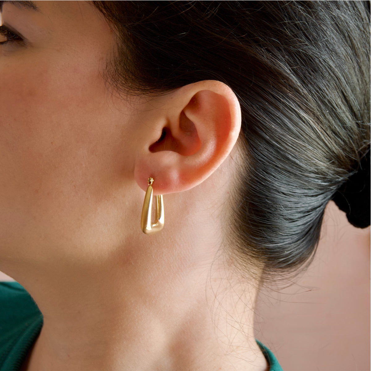 A close-up side profile of a woman wearing a small gold triangular hoop earring.
