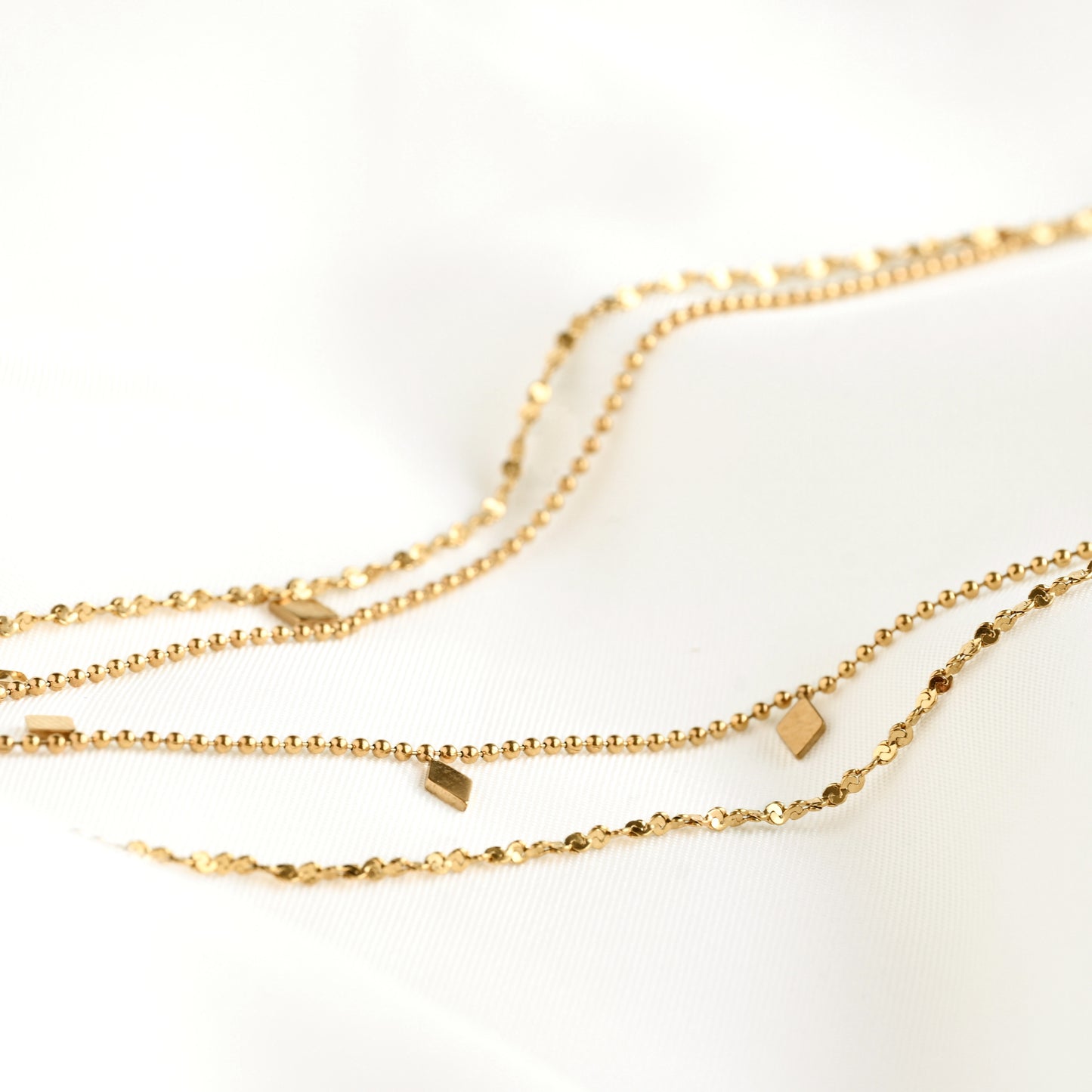 Close up side profile view of layered gold chain necklace with textured chains