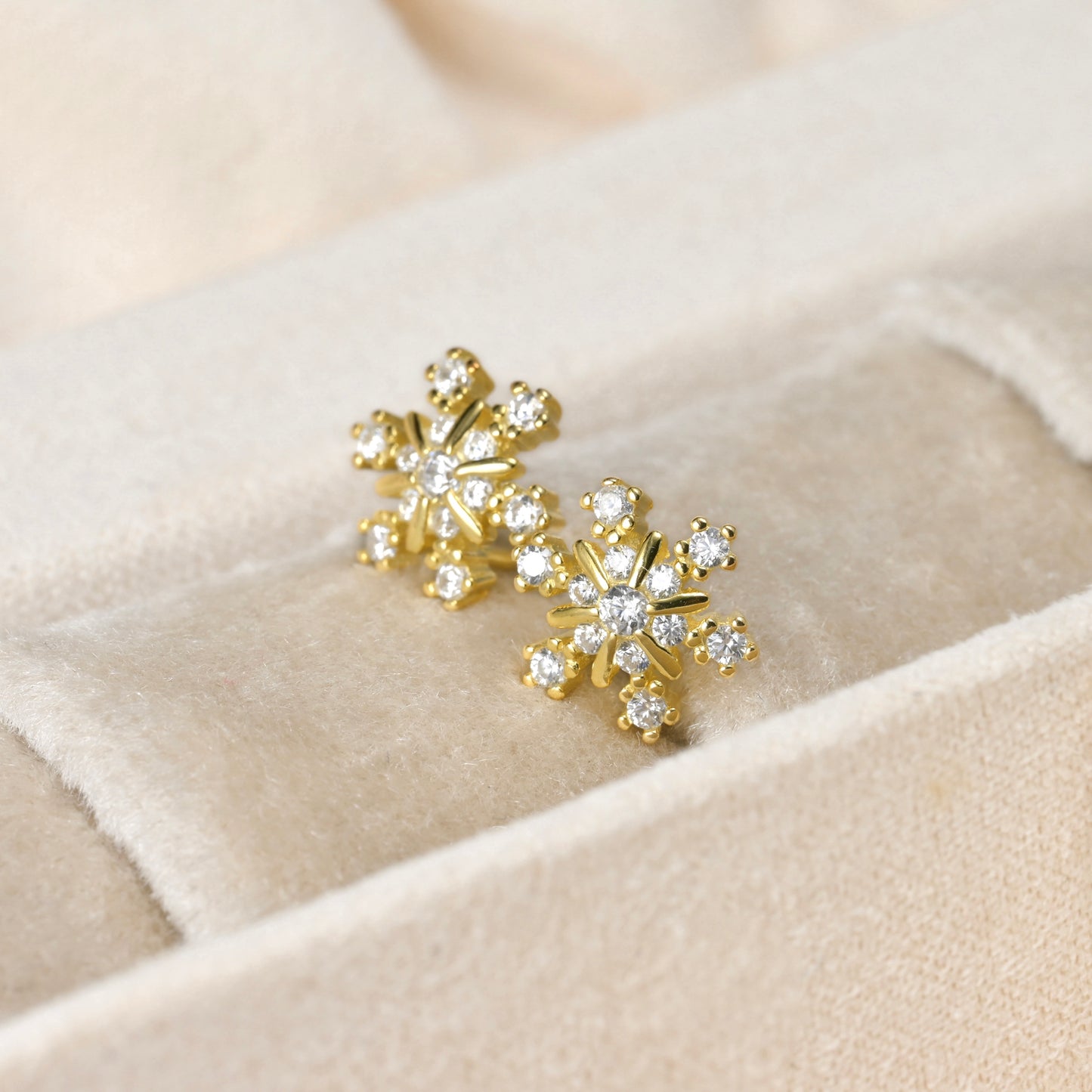 Gold snowflake earrings with clear stones on a beige fabric background