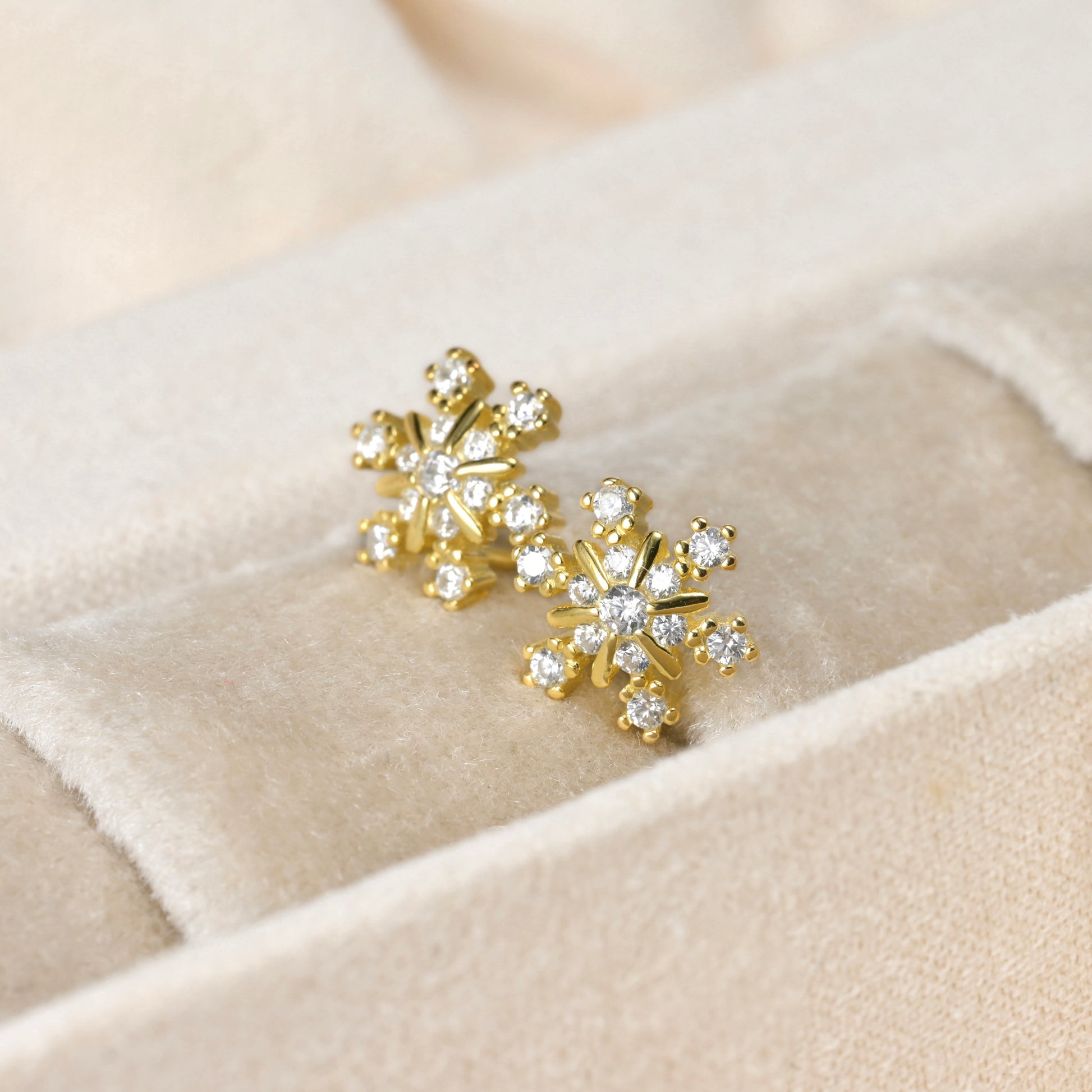 Gold snowflake earrings with clear stones on a beige fabric background