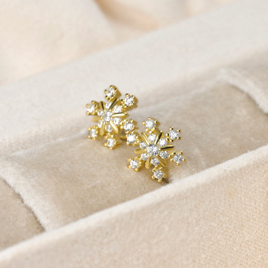 Gold snowflake earrings with clear stones on a beige fabric background