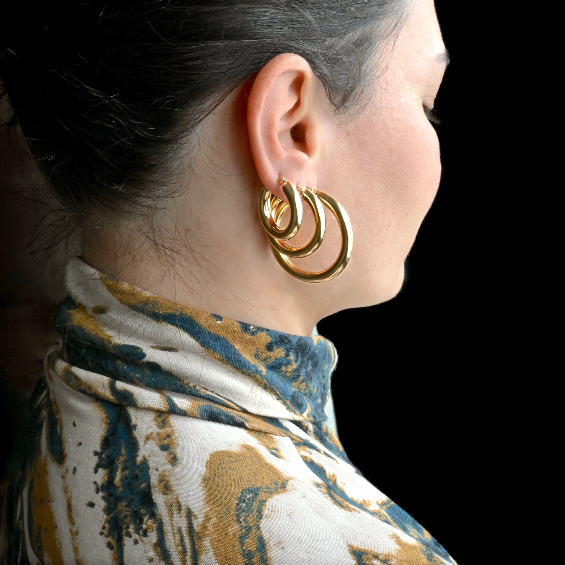 Close-up of a person wearing three thick gold hoops, 25mm, 30mm and 40mm.