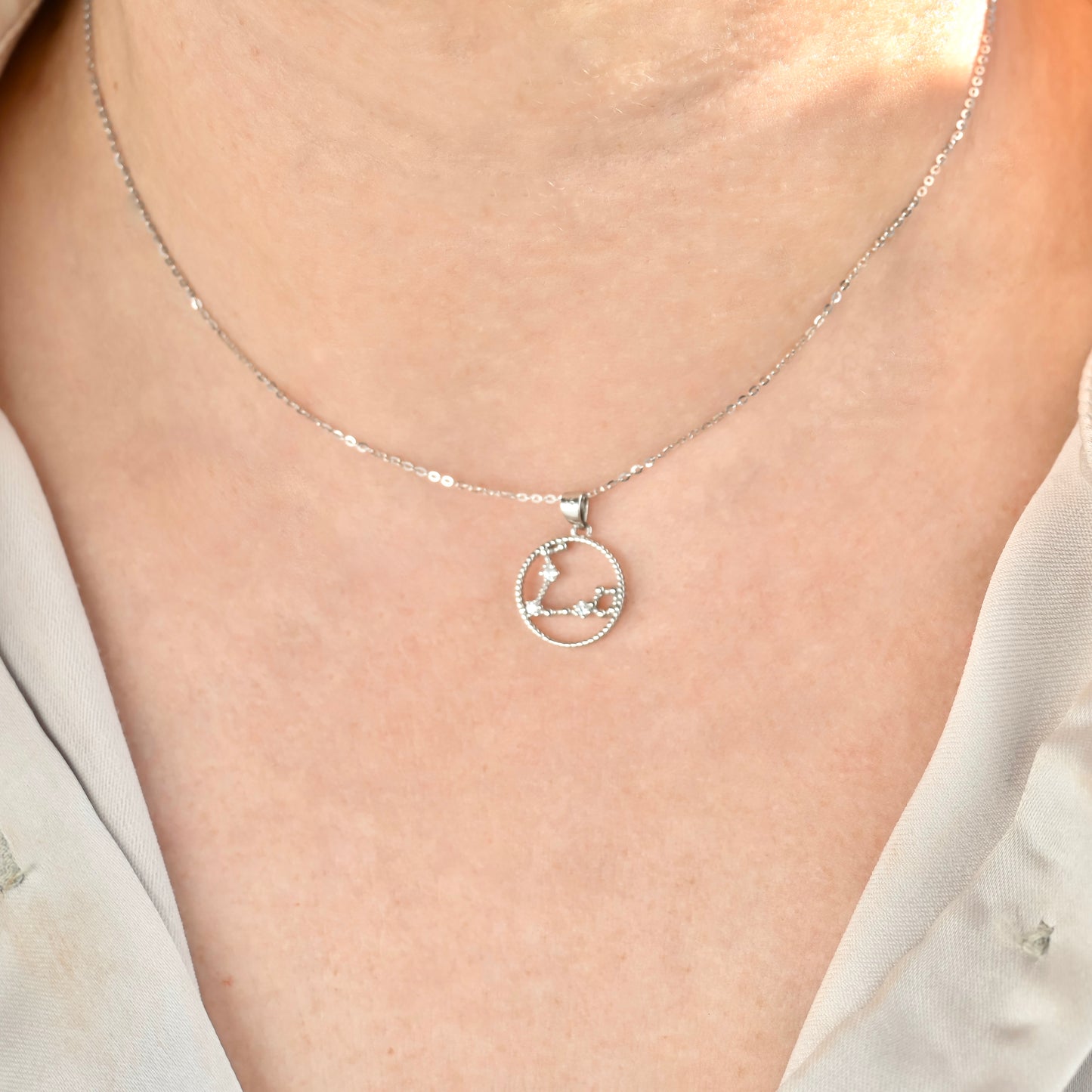 Silver cz constellation necklace with a circular pendant on a person wearing a white shirt.
