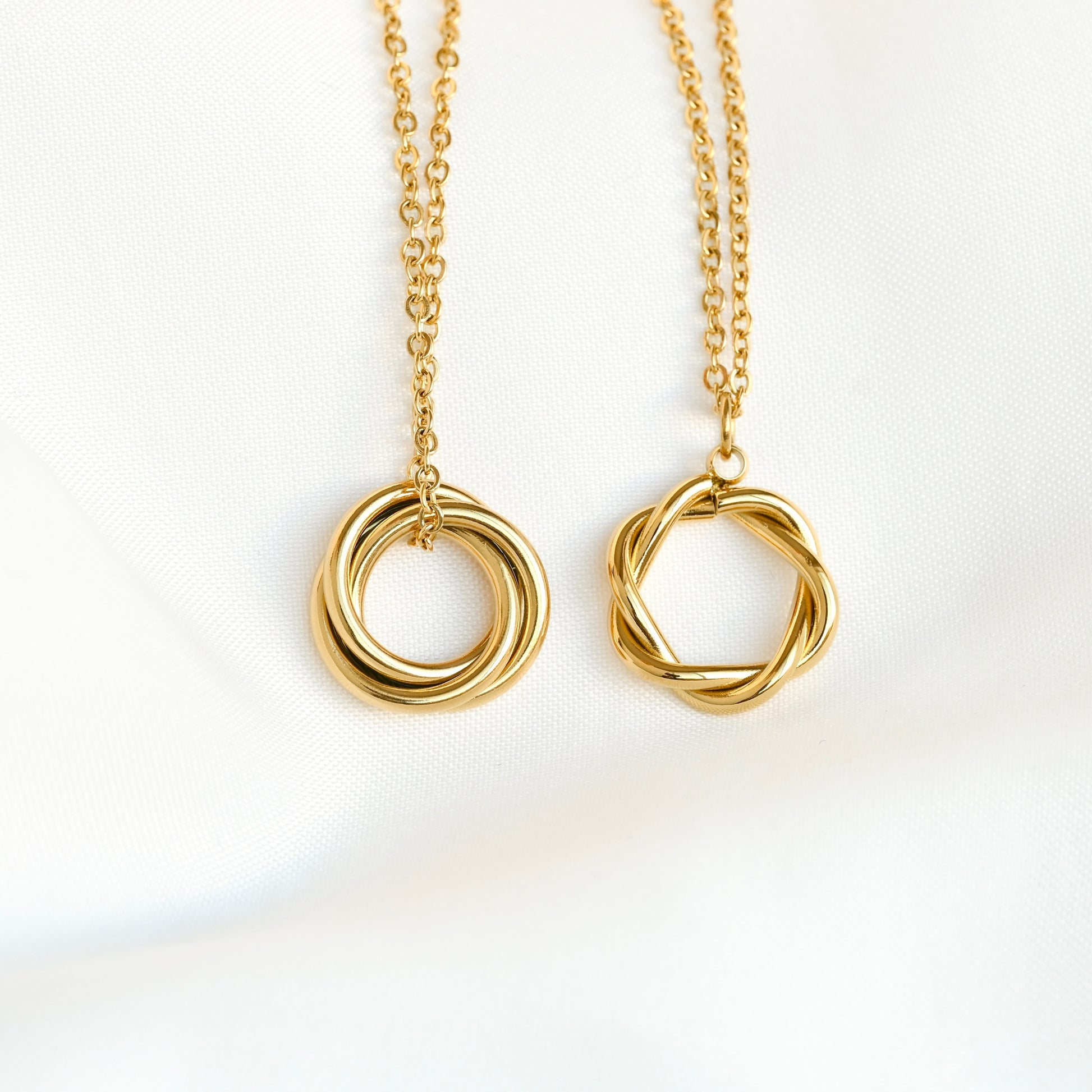 Two gold necklaces with twisted circular pendants on a white background