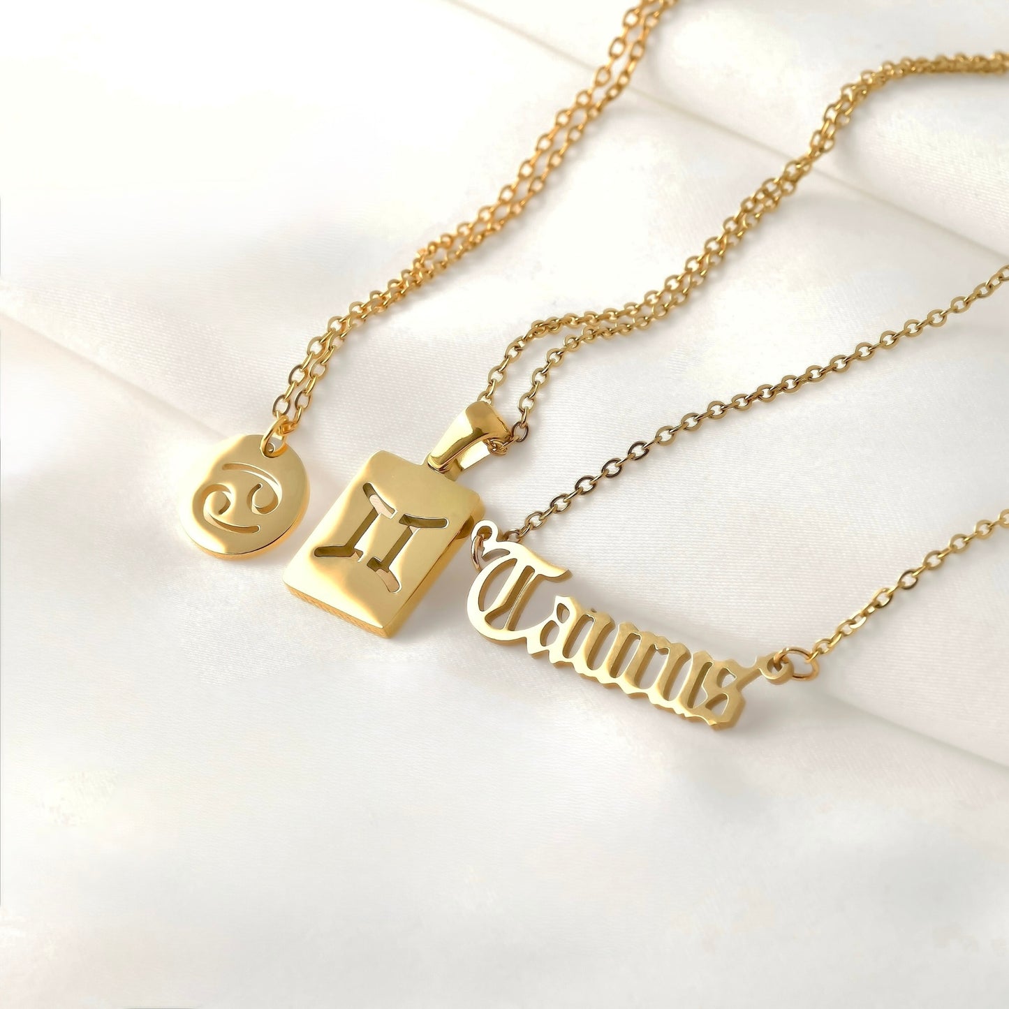 Three gold necklaces with zodiac symbols  with a coin, tag and script pendants, on a white background