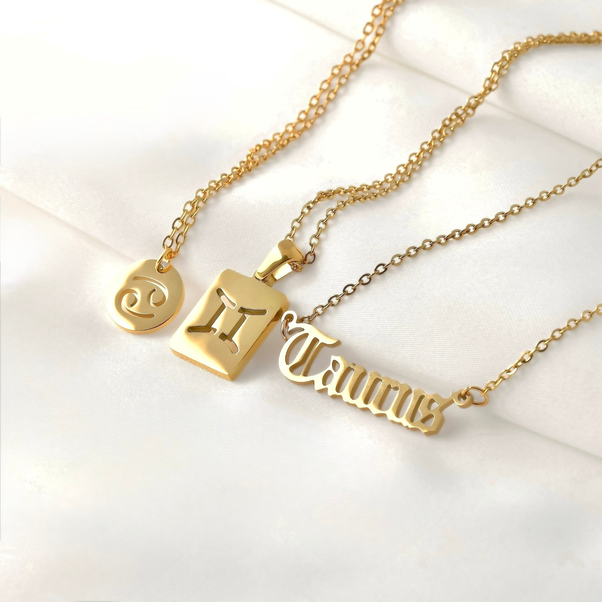 Three gold necklaces with zodiac symbols  with a coin, tag and script pendants, on a white background