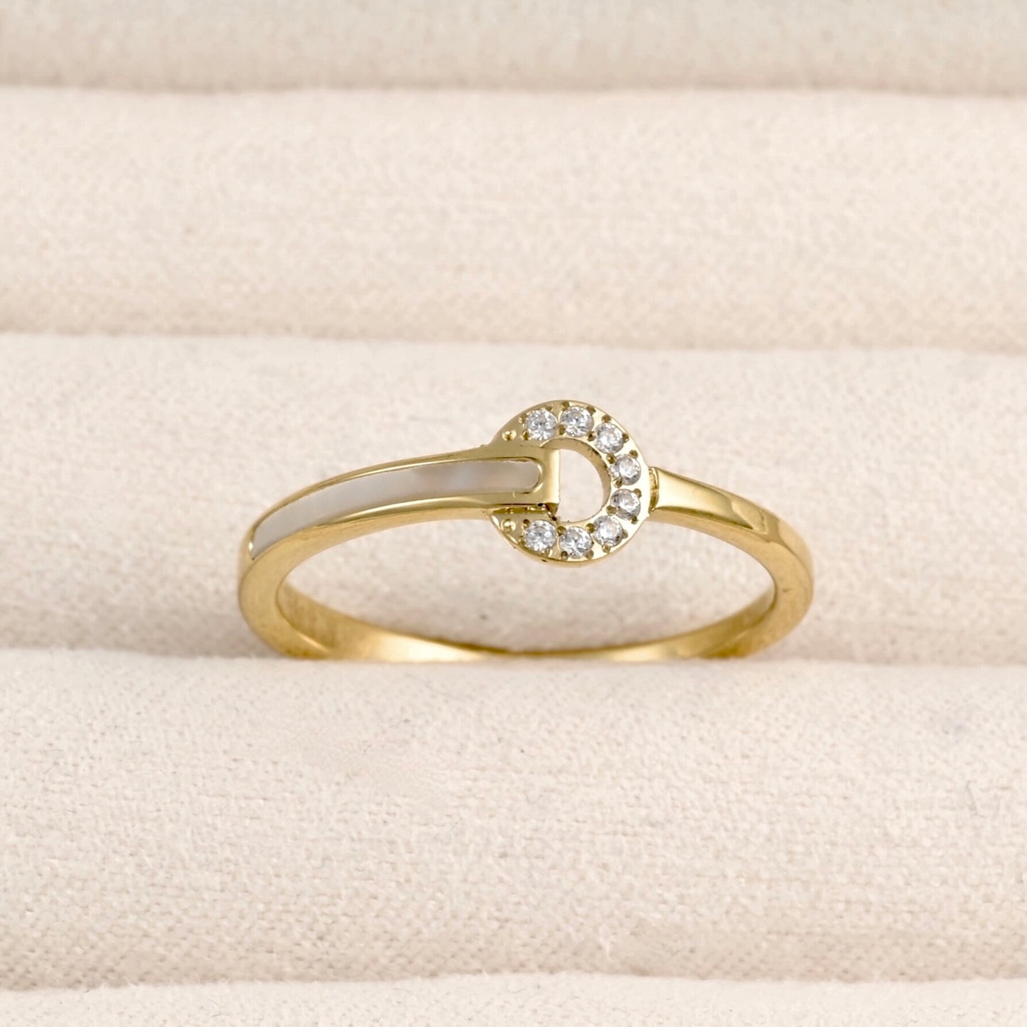 Front view of a delicate gold ring featuring a circle with cz stones shell inlay on the left side of the band, displayed in a beige jewelry box.