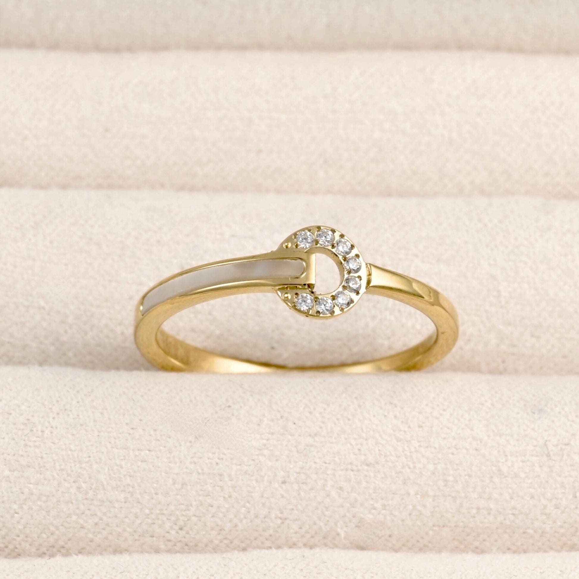 Front view of a delicate gold ring featuring a circle with cz stones shell inlay on the left side of the band, displayed in a beige jewelry box.