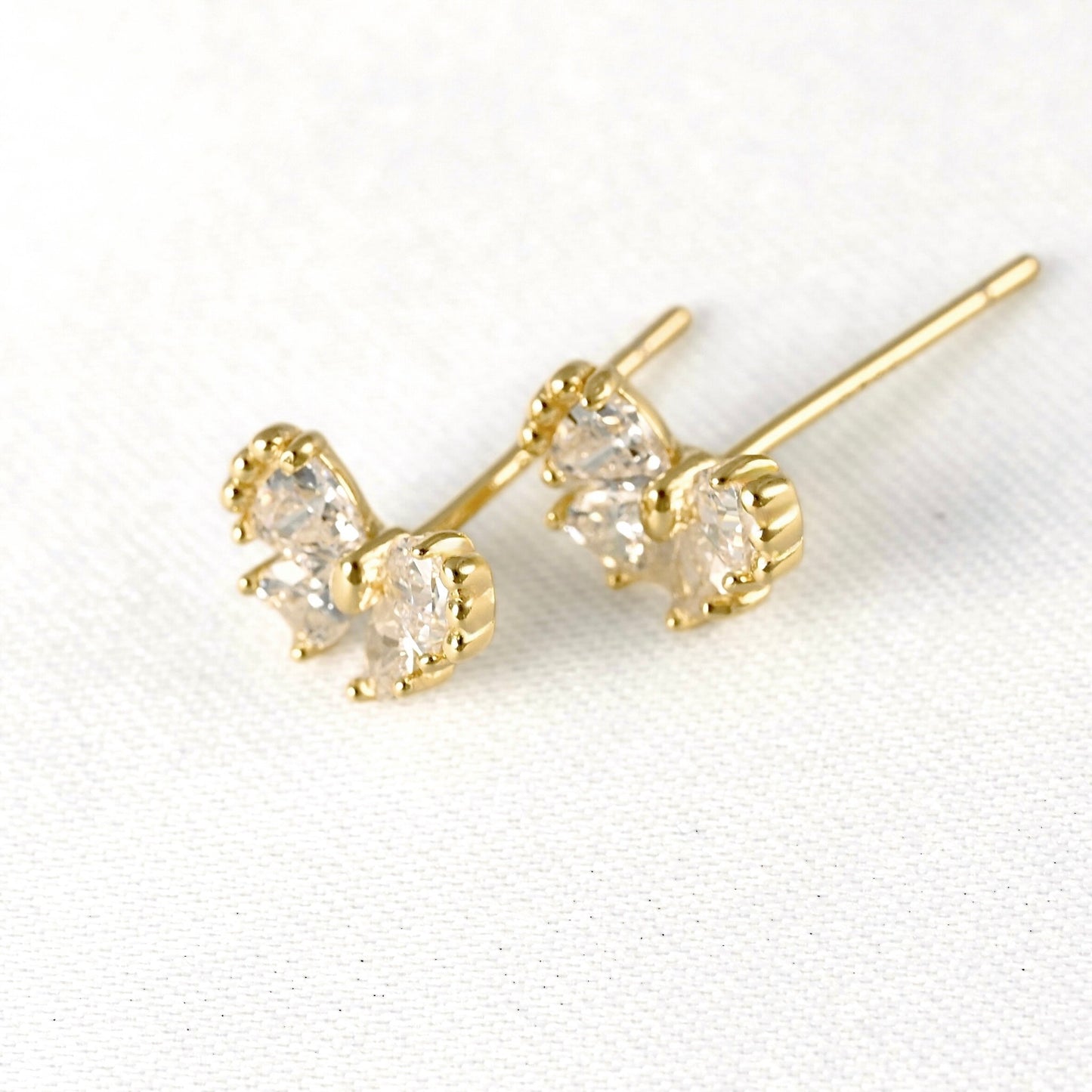 A pair of gold butterfly stud earrings with three clear trillion-cut CZ stones in a prong setting, displayed on a textured white fabric background.