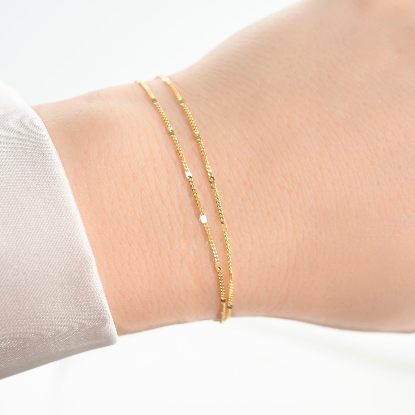 Gold bracelet on a wrist with a plain background