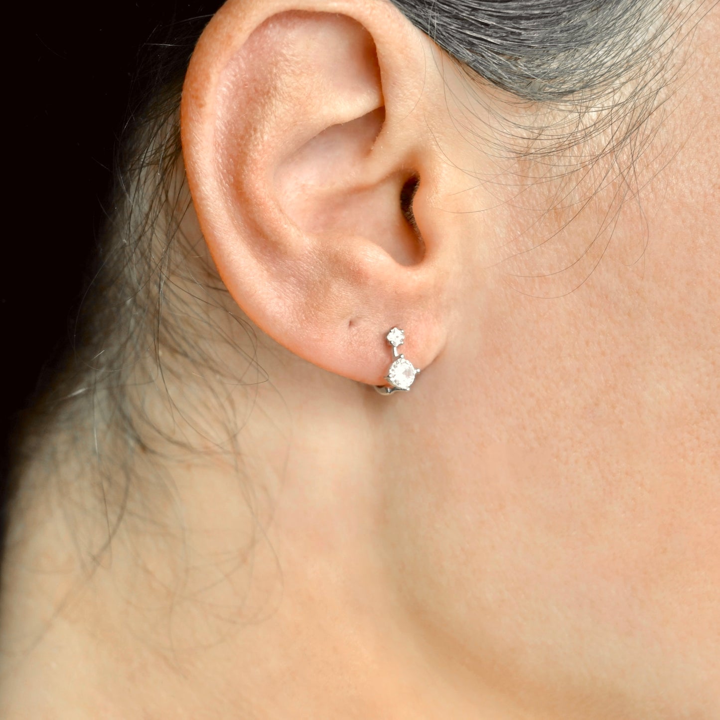 Close-up of an ear wearing a diamond earring with a dark background