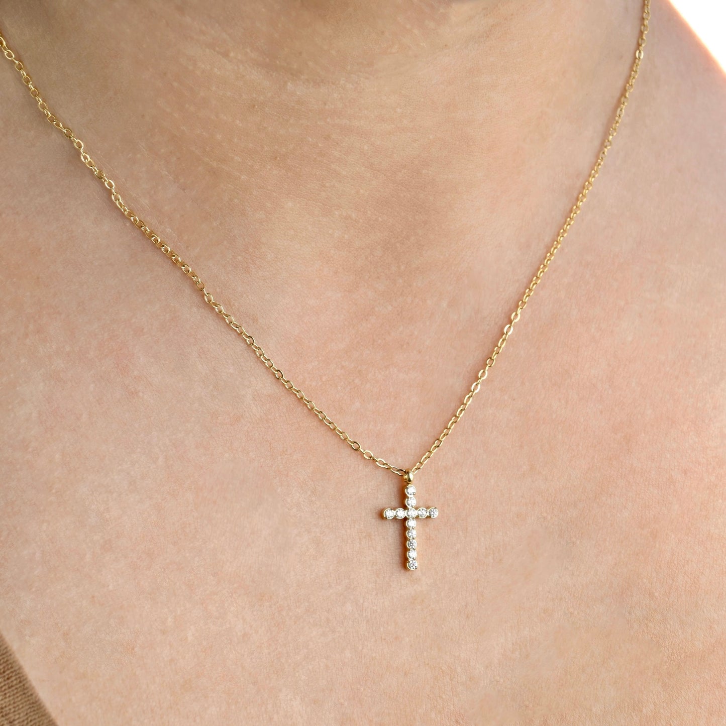 Gold necklace with a  small cross pendant on a person's neck