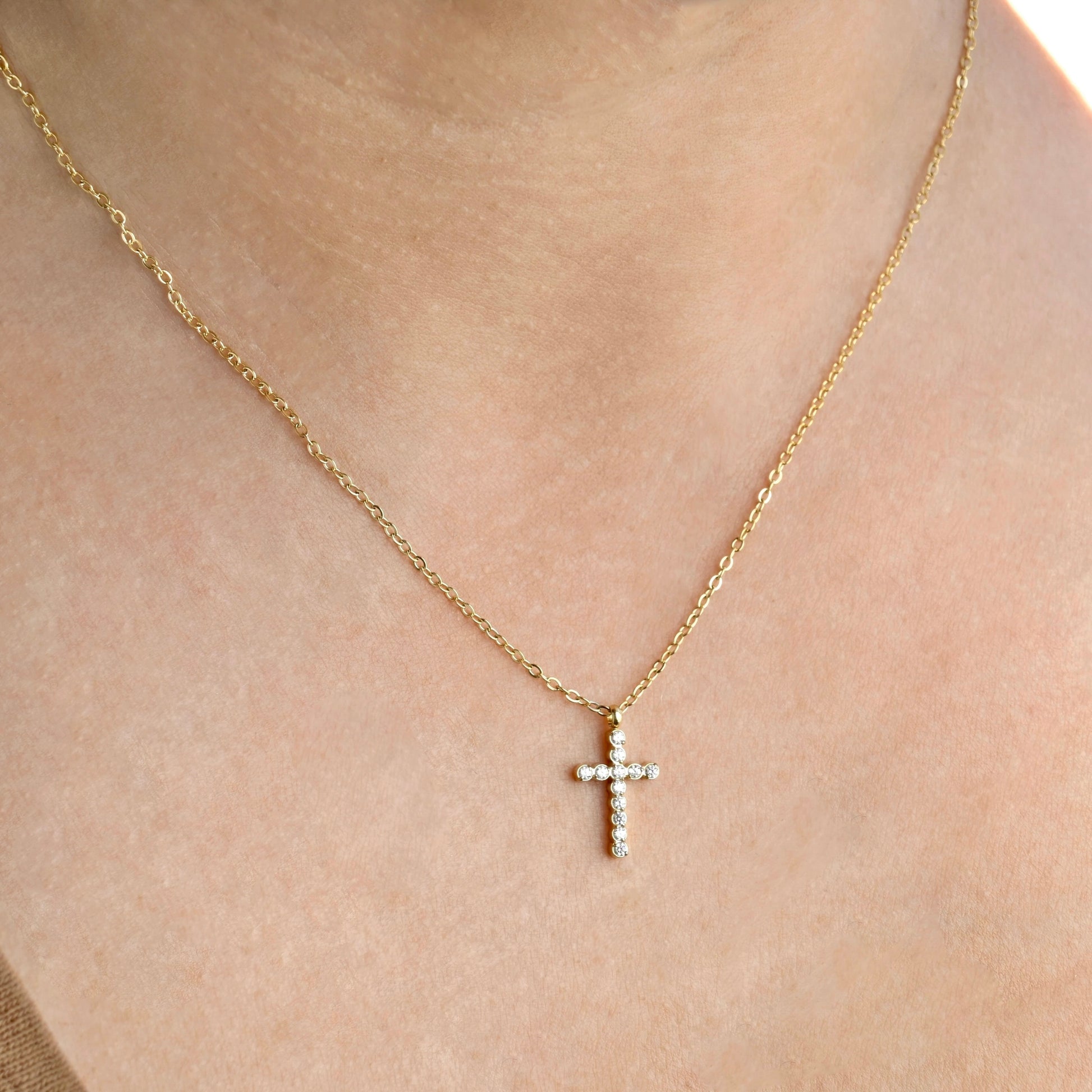 Gold necklace with a  small cross pendant on a person's neck