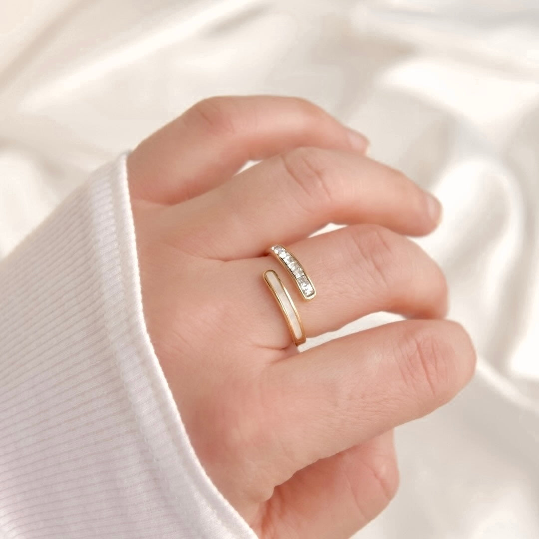 A close-up of a hand wearing a slim wrap ring against a soft white fabric background. O