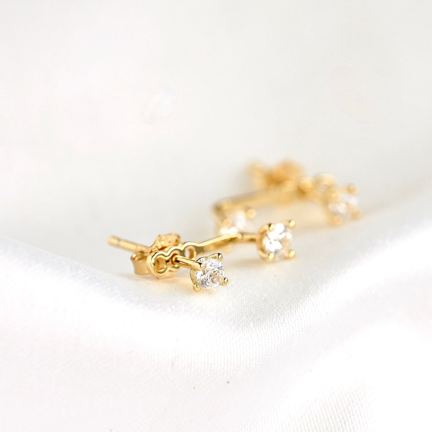 A pair of gold ear jackets with two small round clear stones on  a white backgorund