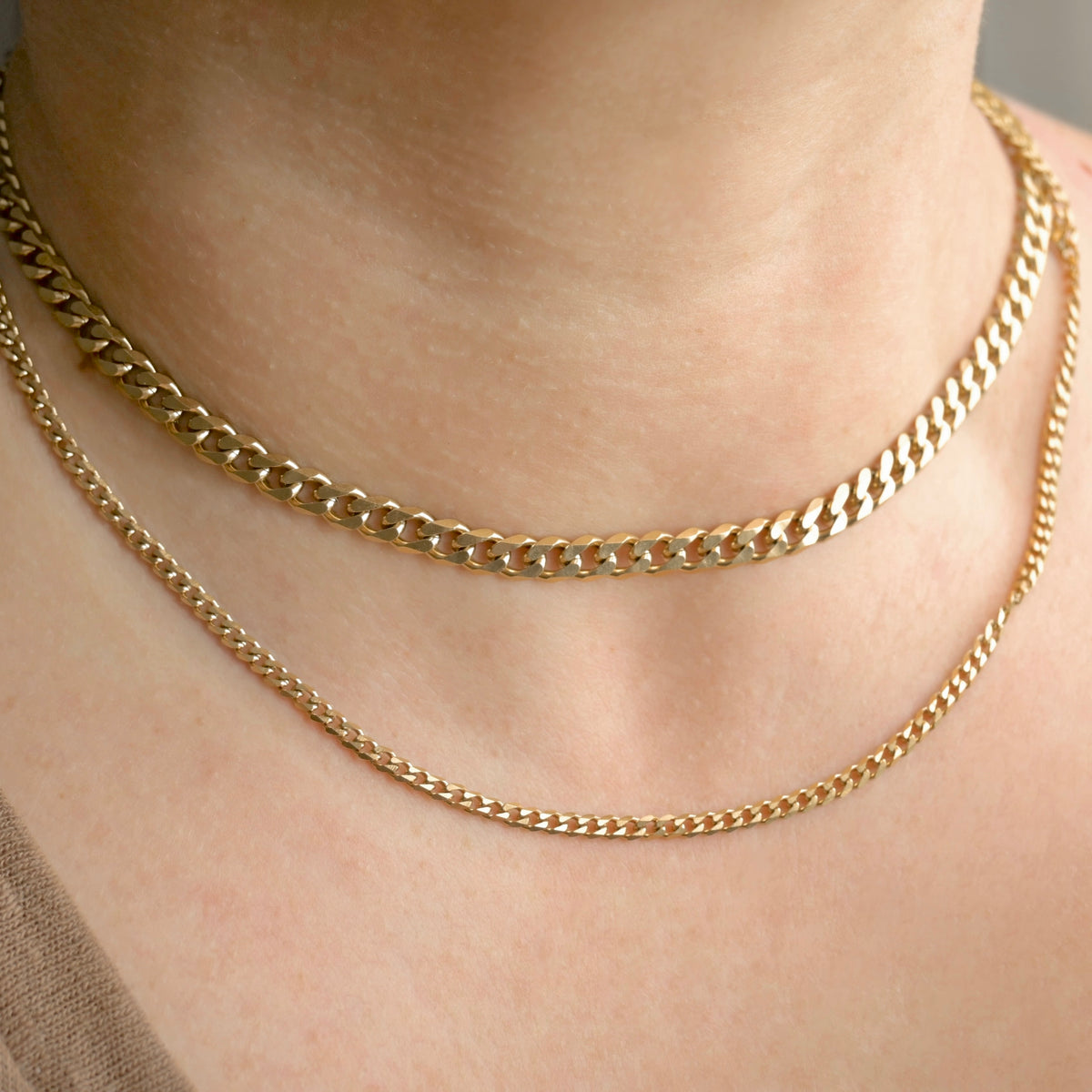 Front view of a person wearing two gold cuban chain necklaces in 3mm, 5mm widths.