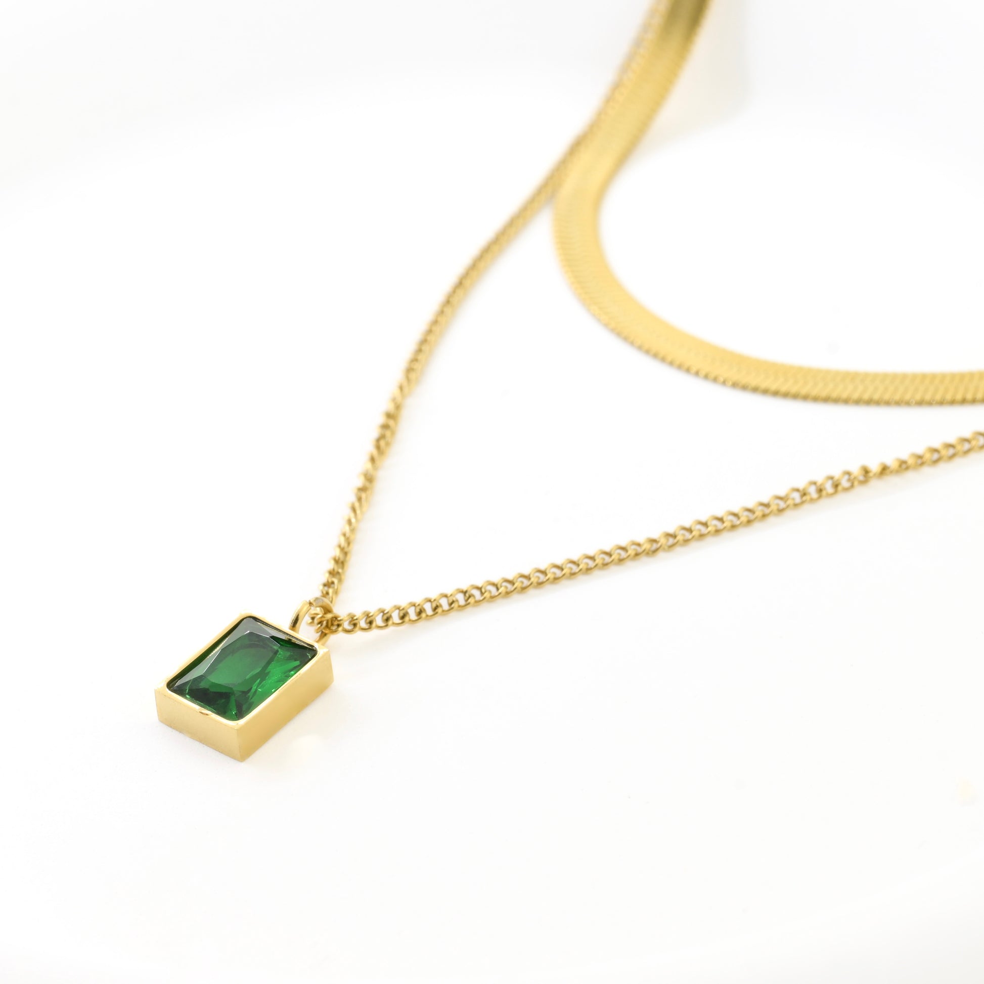 Double layered gold necklace with a green gemstone pendant on a white background