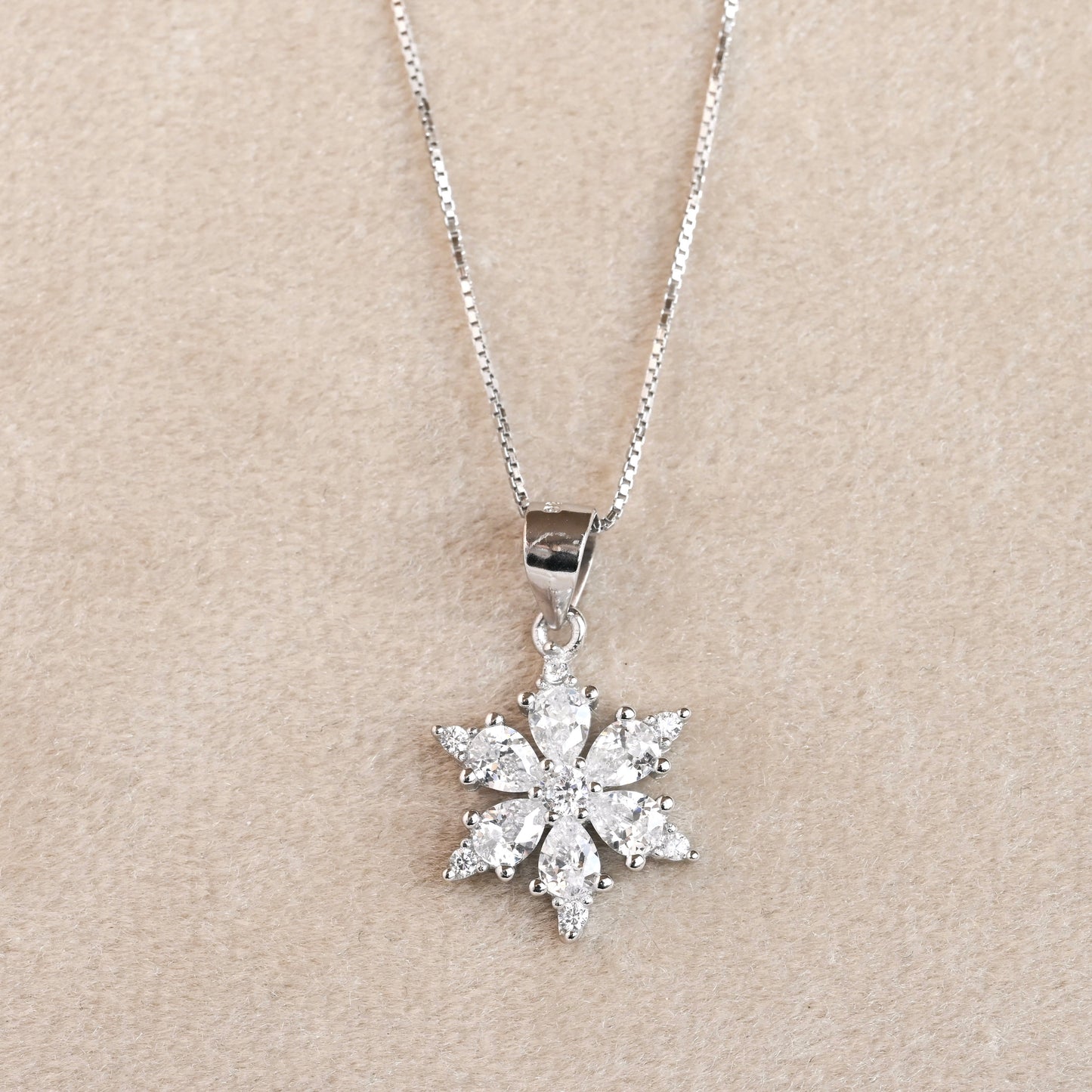 Silver snowflake pendant necklace on a beige background